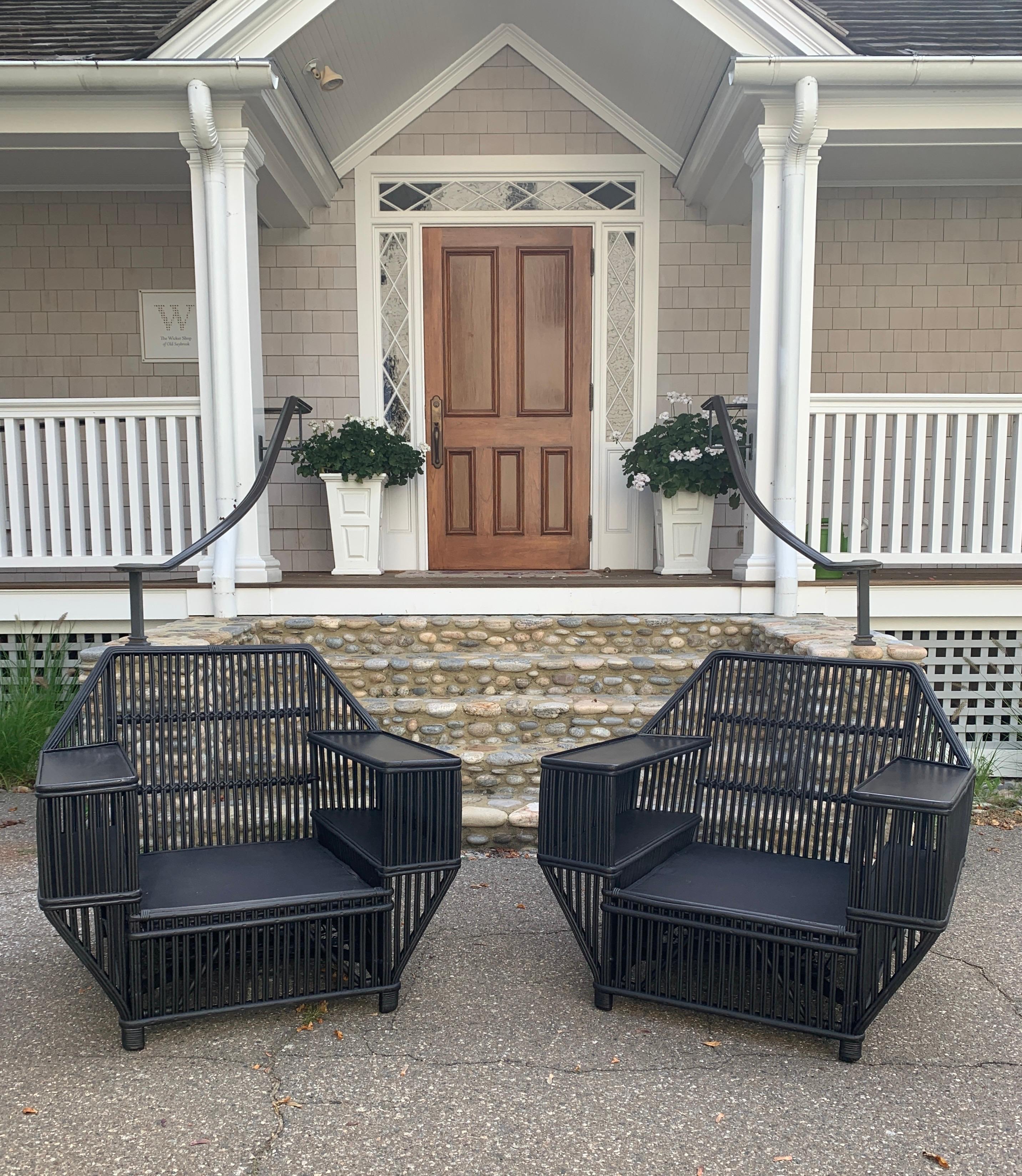 A pair of grand scale stick wicker arm chairs with built in shelves. Seat platform is spring based with fresh black decking. Chairs of this scale are difficult to find.