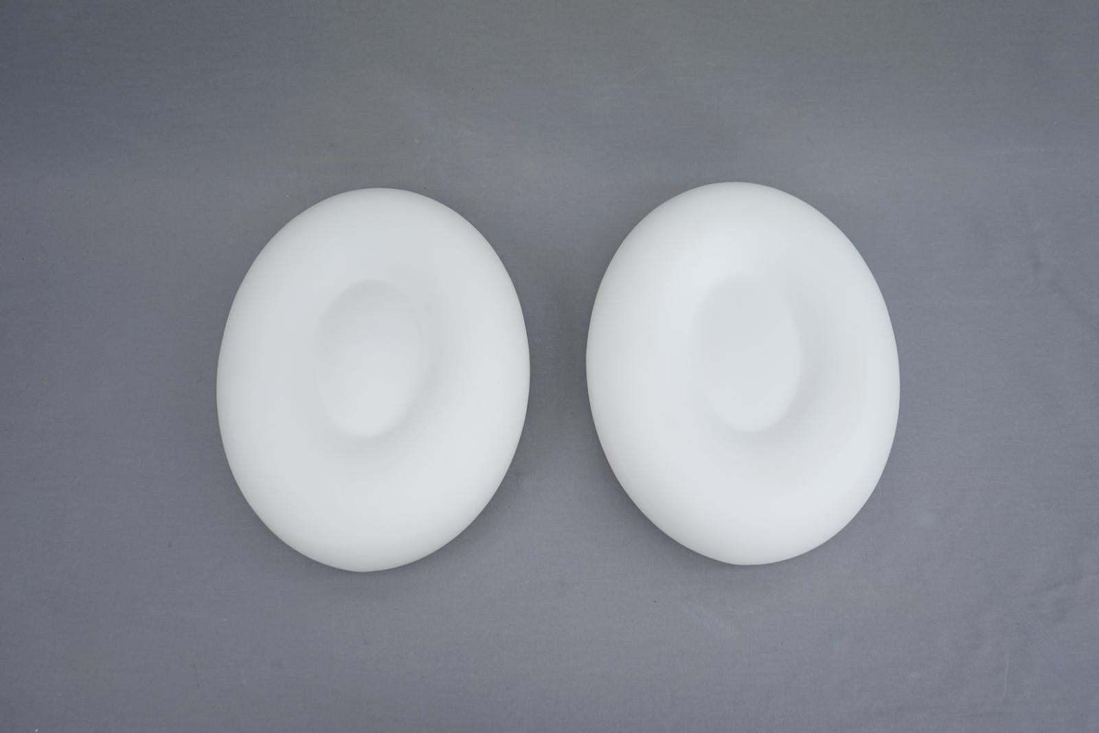 Large stock of white glass wall lamps from a hotel. The lamps were produced in Italy and date back to the late 80s. The lamps are made of white satin glass and have an oval shape. The lamps are fastened with a white metal bracket. The wall lamps can