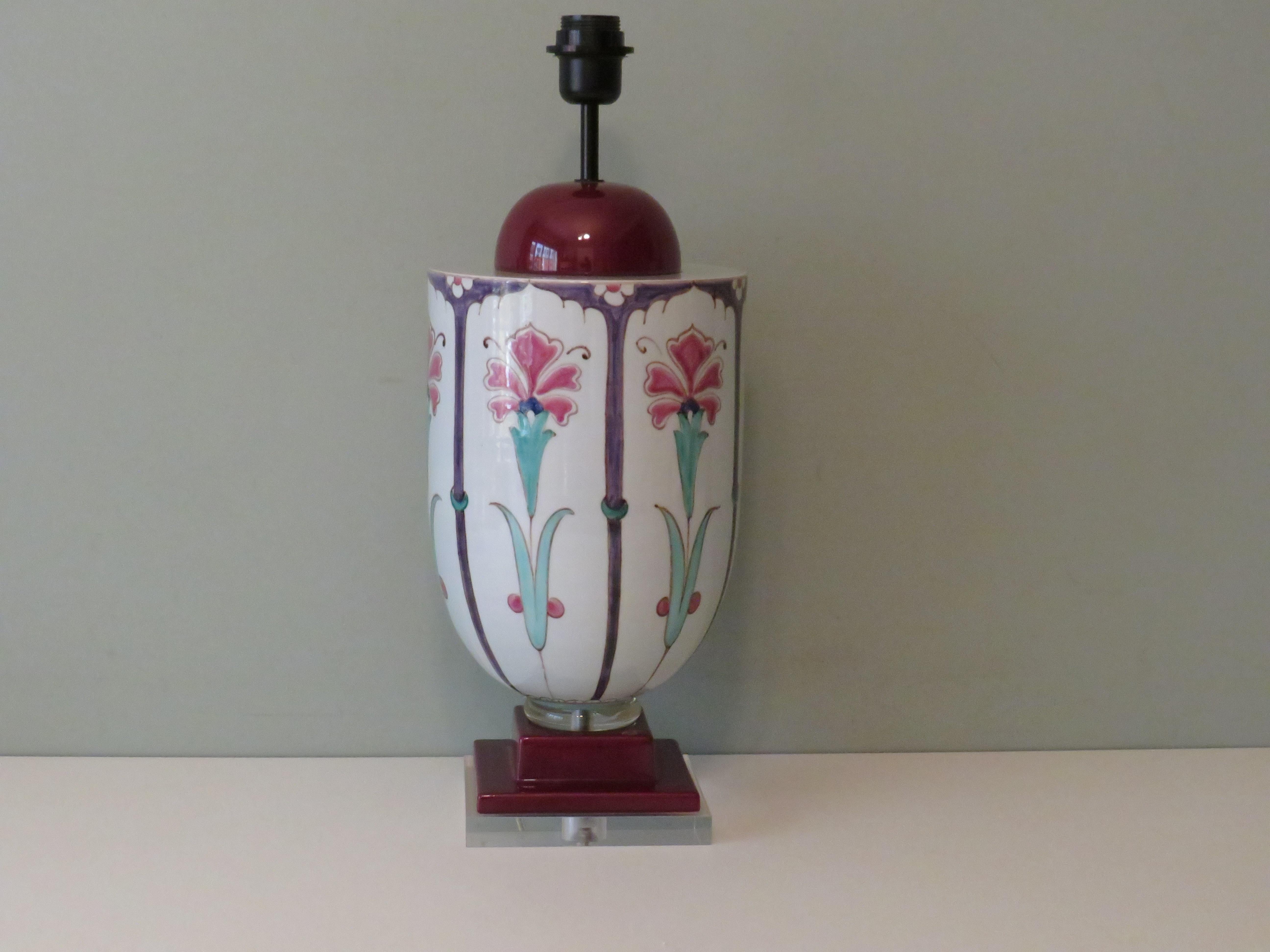 The lamp base with mainly burgundy and white glaze has a hand-painted drawing inspired by the Art Nouveau period in beautiful green and pink tones. The ceramic lamp base is mounted on a square plexi base and has a Bakelite socket with E 27