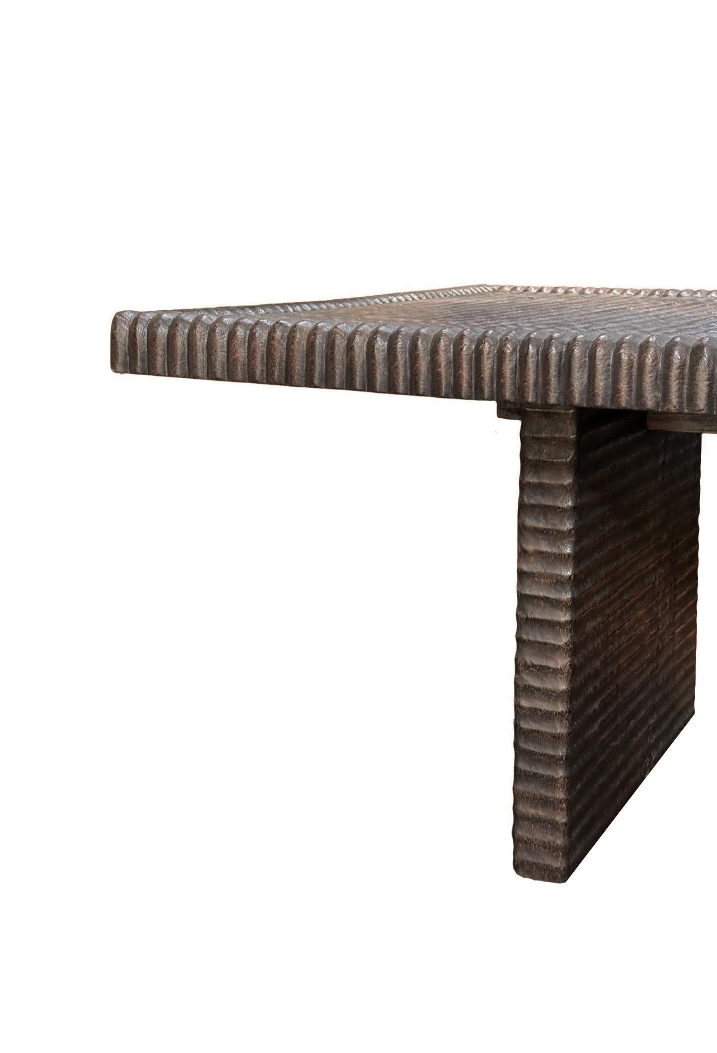 Realizzato in legno massiccio di Suar, questo tavolo da pranzo di grande impatto è un'audace miscela di forme naturali e raffinata maestria. Il piano del tavolo, di dimensioni generose, presenta intricati dettagli lineari intagliati a mano che