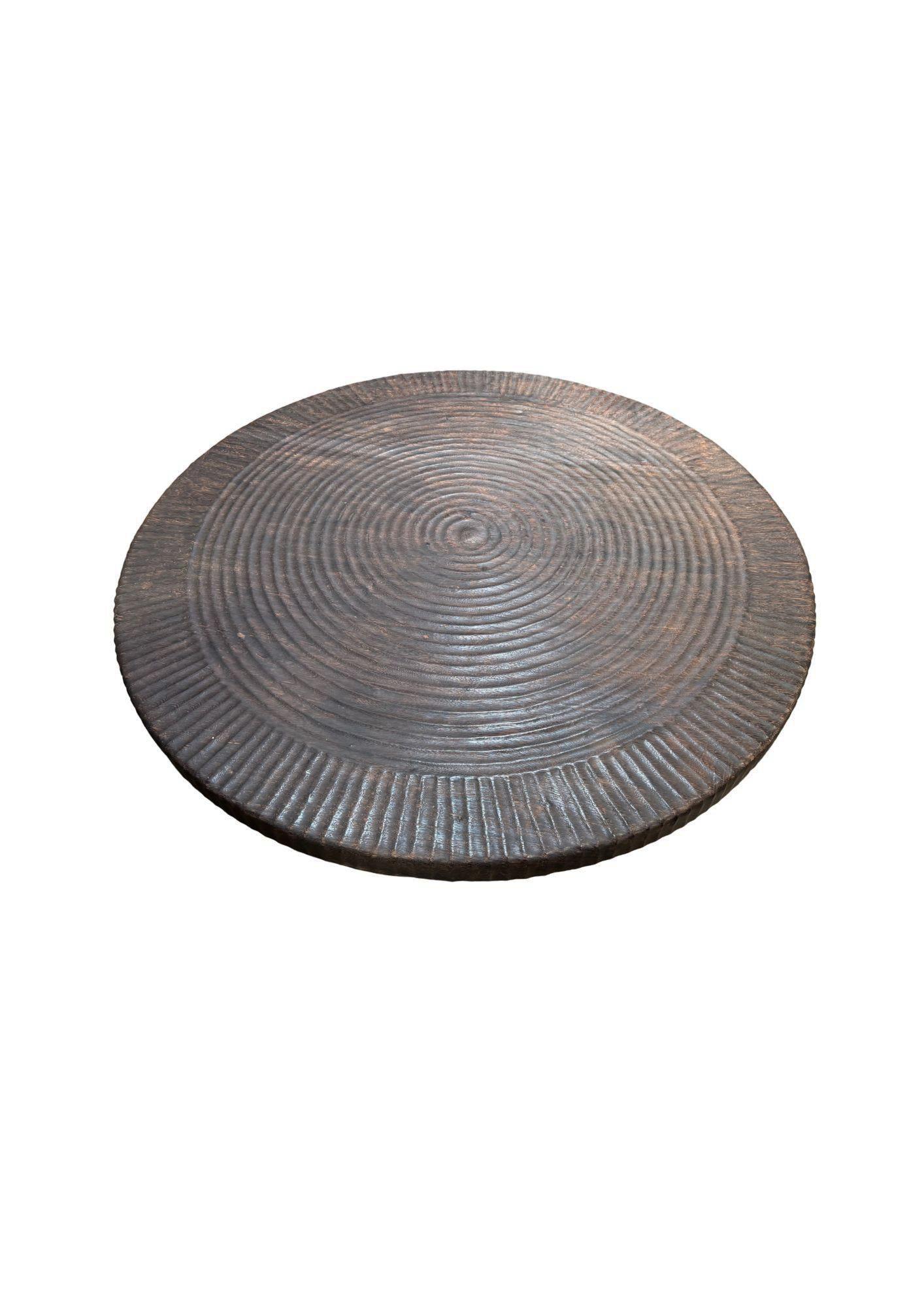 Questo tavolo rotondo di grandi dimensioni è un vero e proprio pezzo forte, realizzato in legno massiccio e rifinito con una ricca tonalità marrone scuro espresso. Il piano del tavolo presenta intricati dettagli intagliati a mano che si irradiano