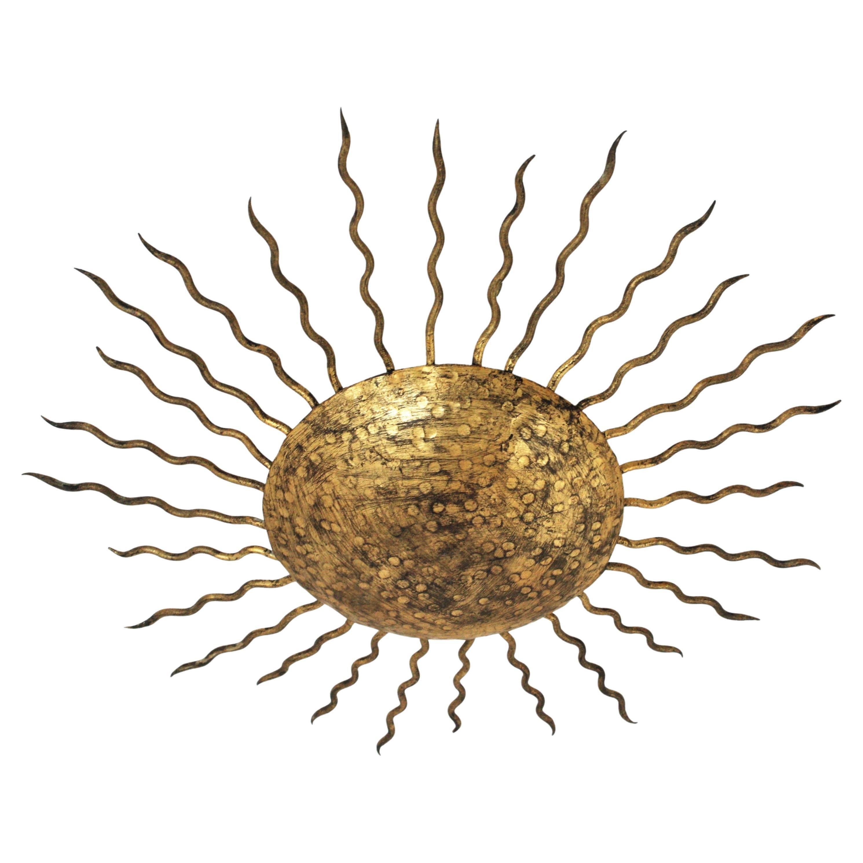 Gold leaf gilt wrought iron sunburst flush mount, Spain, 1950s.
Large Hand-hammered sunburst light fixture richly decorated in the central part by the hammer marks. Curly iron rays surrounding the central sphere.
Original gold leaf gilding and