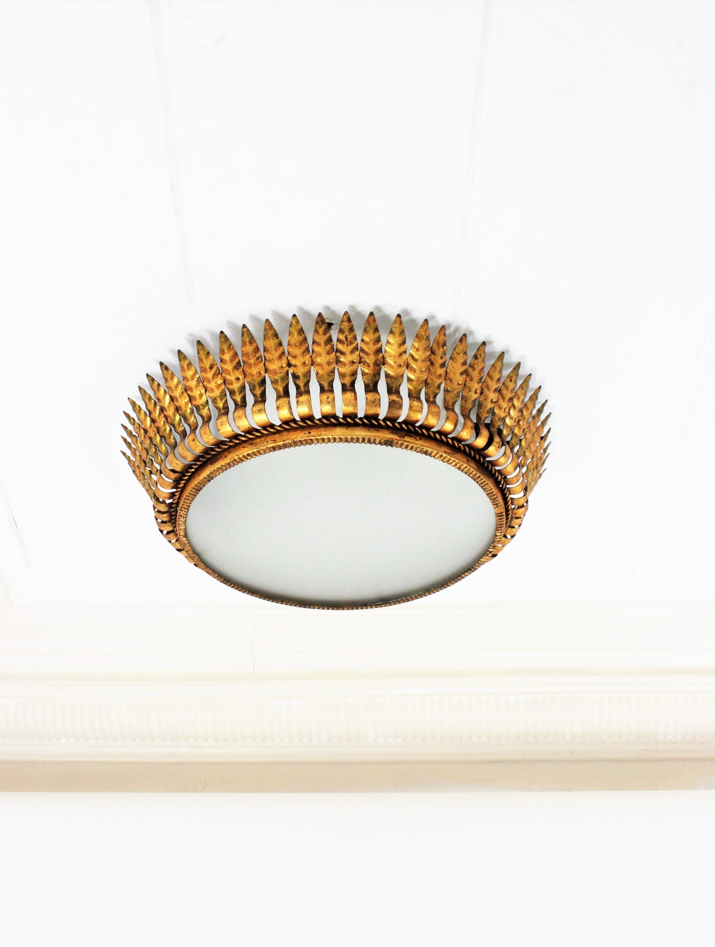 Midcentury Crown Sunburst Large Flush Mount (54 cm ), Gilt Iron, Frosted Glass, Spain, 1950s.
This sunburst flushmount or pendant has leaf motifs surrounding a central frosted glass diffuser and a twisted iron rope surrounding the