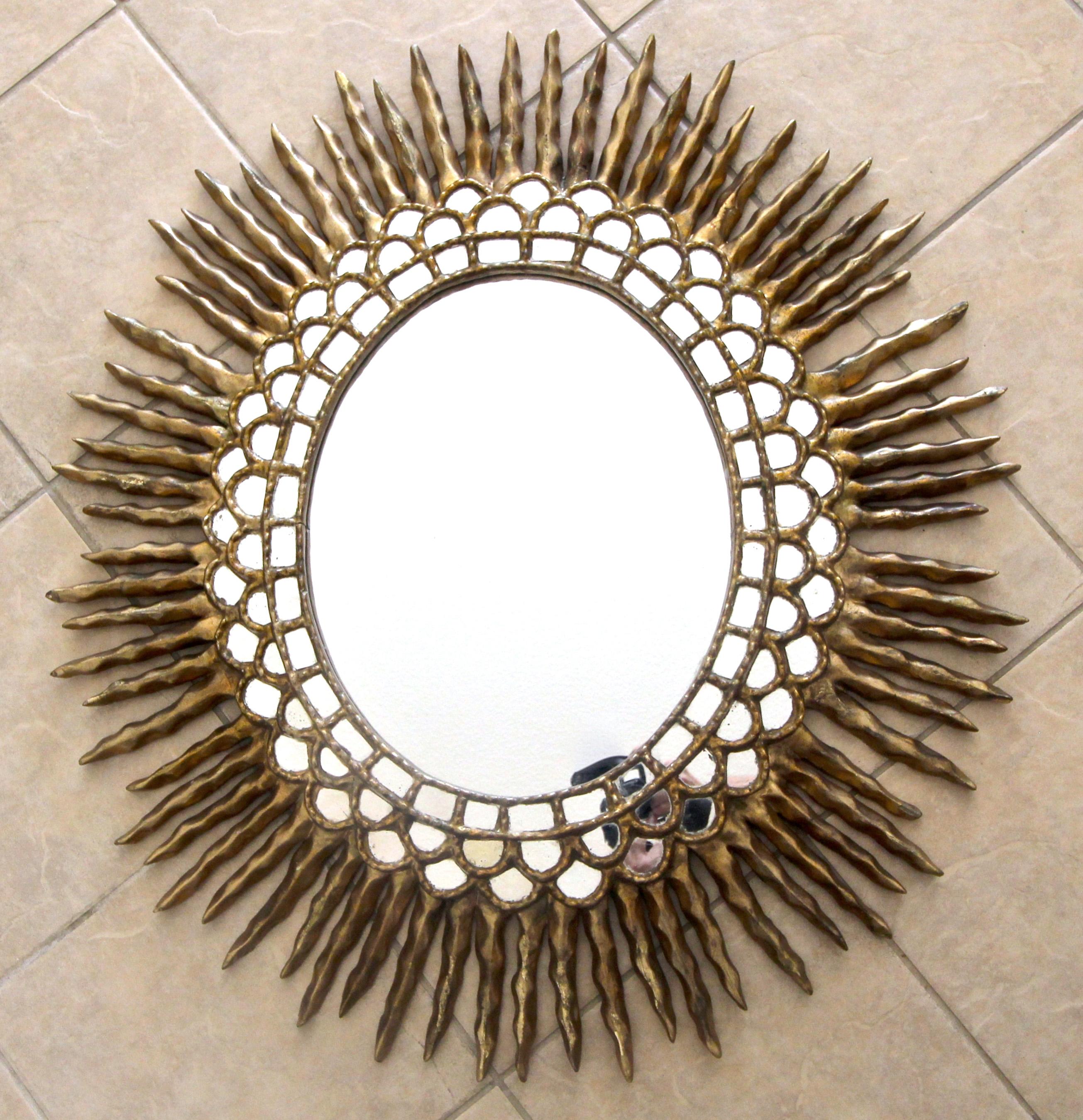 Huge hand-carved oval shaped colonial Spanish style wall mirror in gold gilt finish. Smaller rows of small inset mirrors encircle the large central mirror, and outer carved giltwood extended spikes or rays. 

Measures: 38