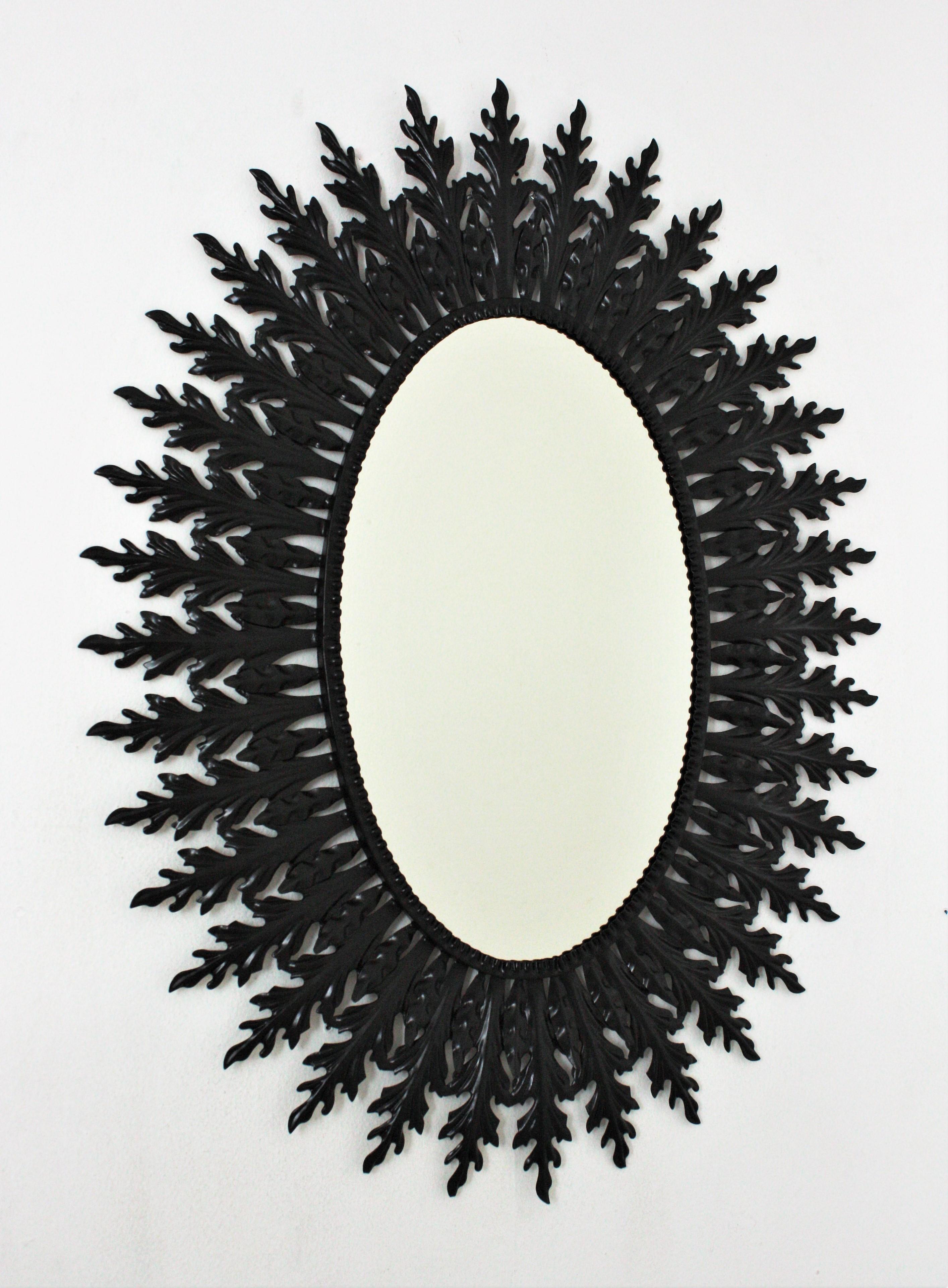 A huge oval sunburst mirror handcrafted in metal with black painted finishing, Spain, 1960s.
The frame of this oval mirror has a layer or large leaves and a layer of small leaves surrounding the glass.
This iron sunburst mirror has been finished
