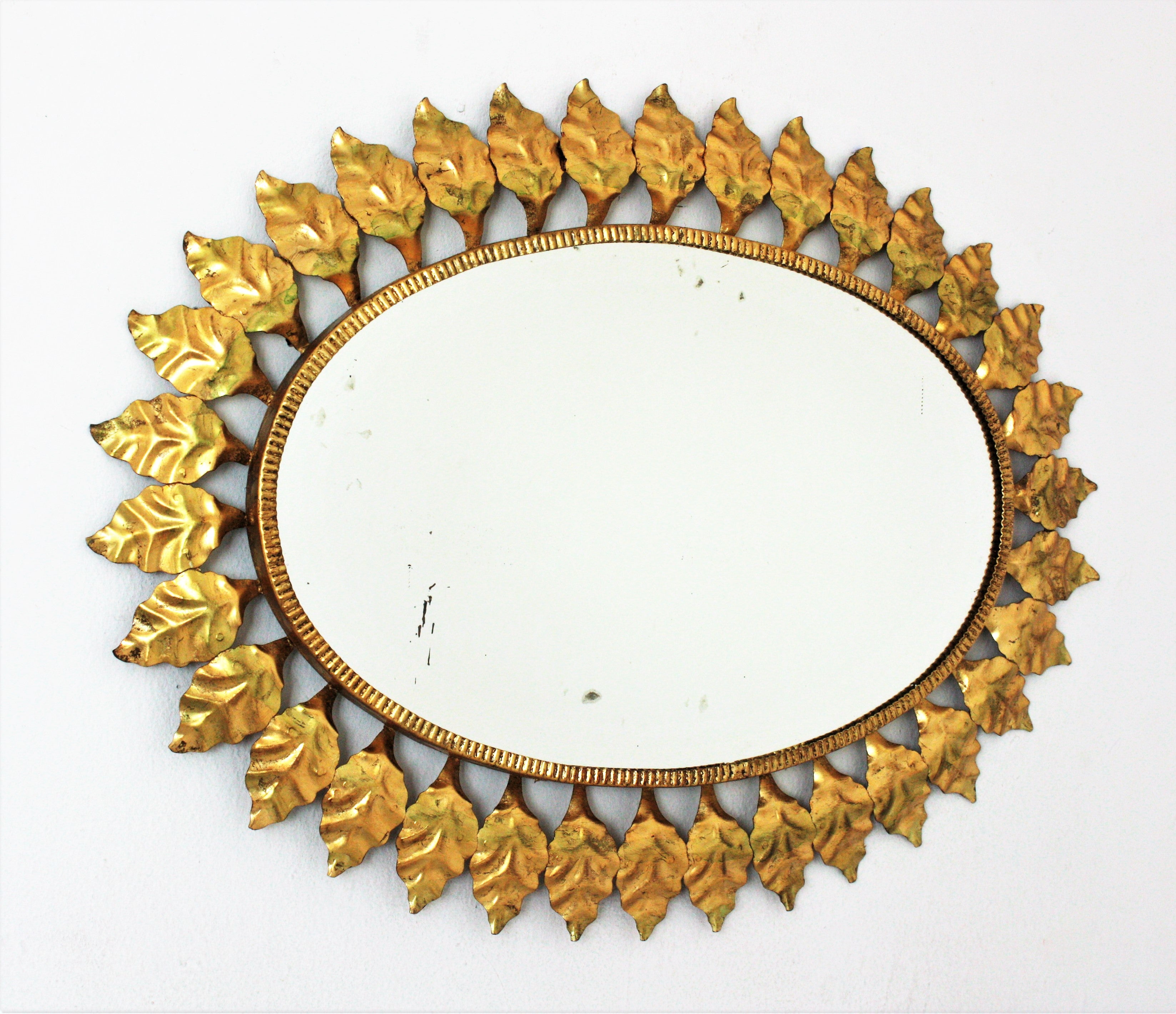 Large Mid-Century Modern wrought iron sunburst oval wall mirror with gold leaf finish, Spain, 1950s.
This highly decorative leafed sunburst gilt iron mirror has a nice color. It has terrific aged patina showing its original gold leaf gilding.
A