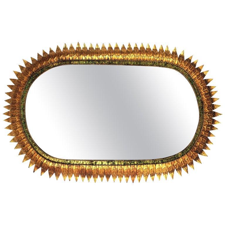 Oval sunburst mirror, gold leaf gilt and green iron, Spain, 1950s.
Hand-hammered iron oval sunburst wall mirror with gold leaf finish and green patinated details.
It has a gilt green patinated ring surrounding the glass
Its highly decorative