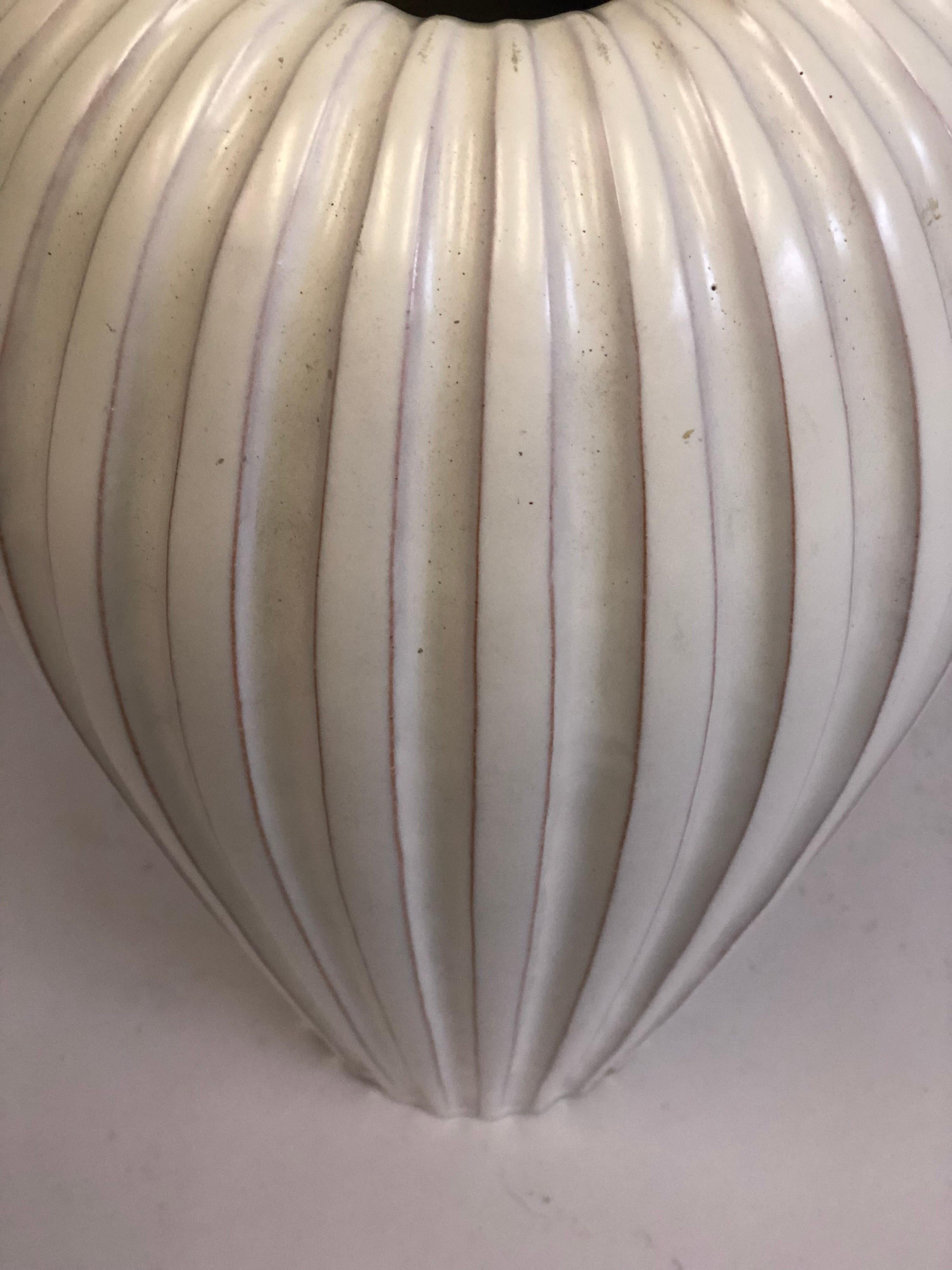 Large Swedish Mid-Century Modern white ceramic table lamp base / vase designed by Vicke Lindstrand for Upsala Ekeby. The form of the piece is elegantly conceived; it is tapered and fluted. The under glaze of the white exterior has burnt reddish