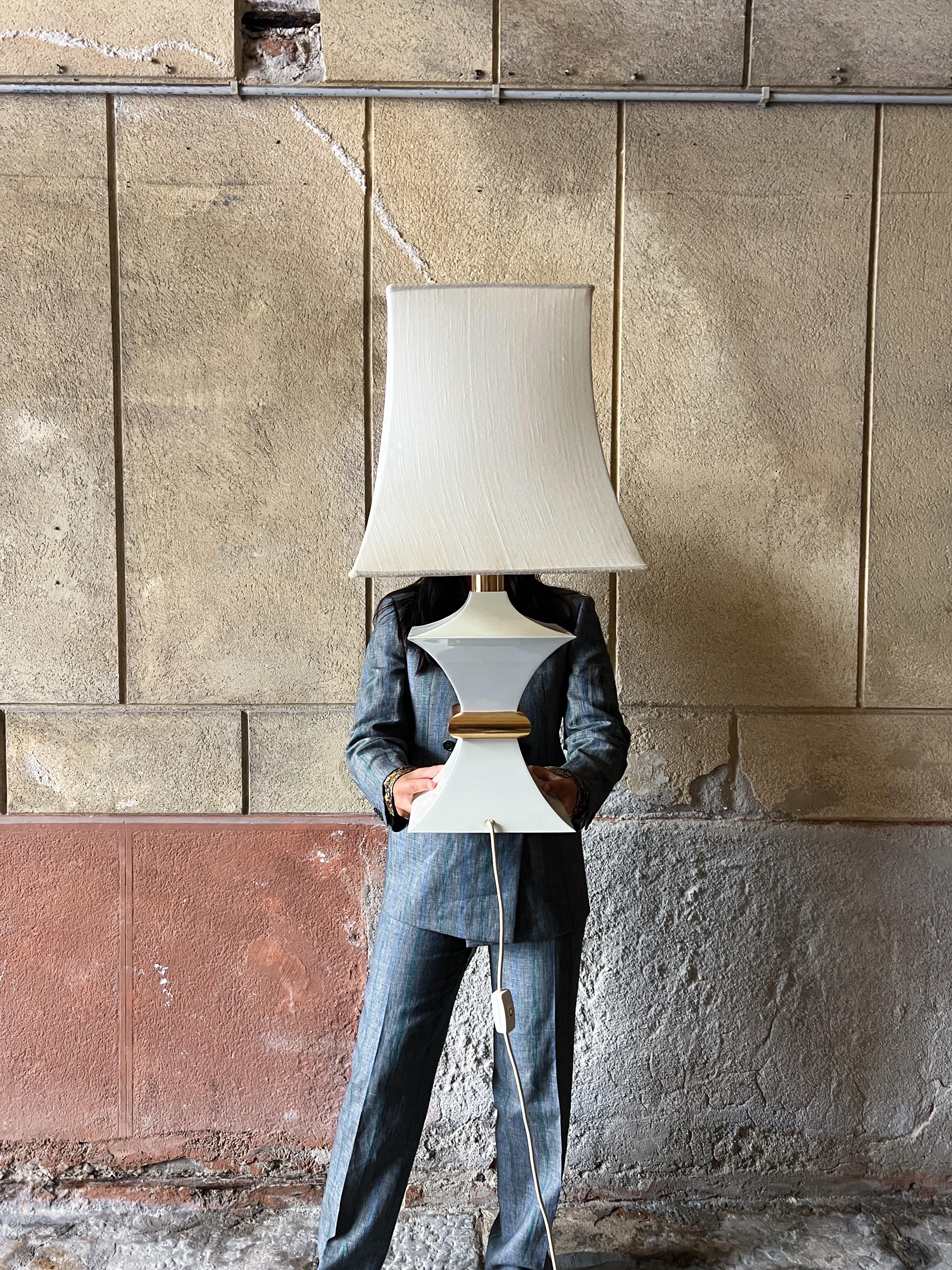 Exquisite large table lamp, crafted in Italy during the stylish 1970s, this lamp is a true testament to Italian design elegance.

Meticulously fashioned from cream-coated metal and adorned with a gleaming golden brass accent at the center. Its