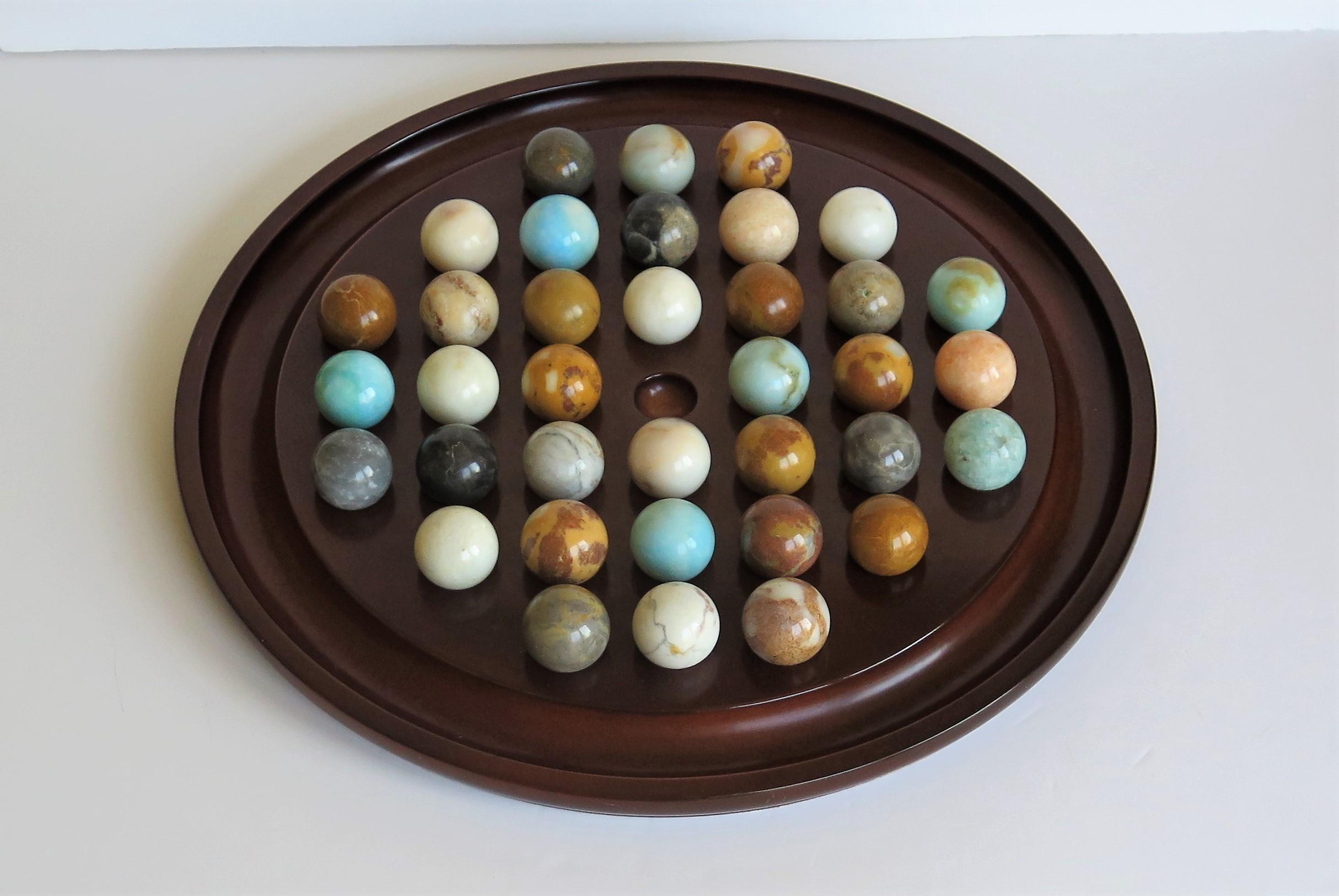 This is a very decorative and complete board game of 37 hole marble solitaire with a very large 13.5 inch diameter board and 36 beautiful individual large agate or mineral stone marbles, which we date to the mid-20th century, probably of French