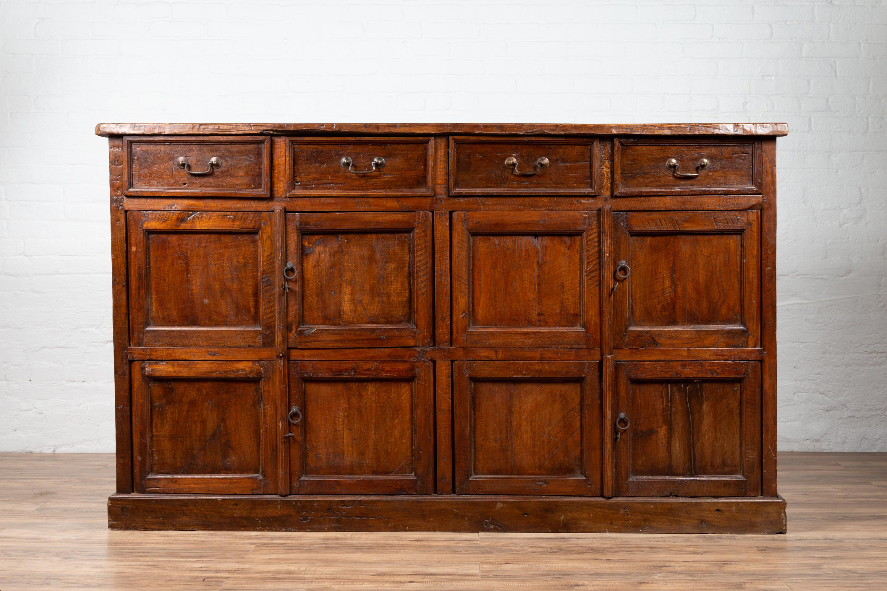 A large Javanese teak cabinet from the early 20th century, with four drawers, and four sets of double doors. Born on the island of Java in the early years of the 20th century, this robust teak cabinet features a rectangular top sitting above four