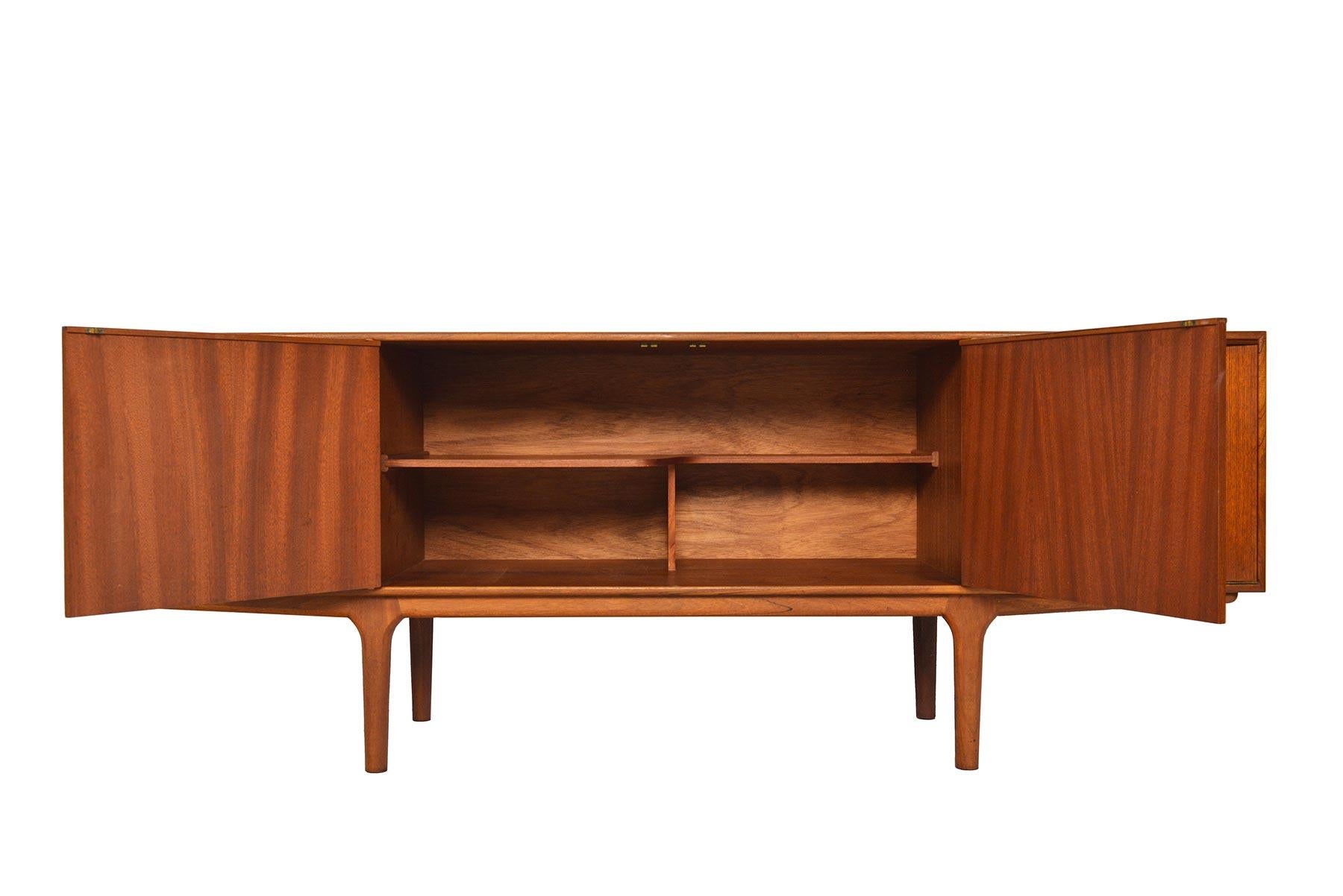 This Mid-Century Modern large low line teak sideboard by A.H. McIntosh is from the Dunvegan Range. Two center doors open to reveal a fixed asymmetrical bar shelf. Right bar cabinet drops down to reveal open storage, and a slide out laminated drink
