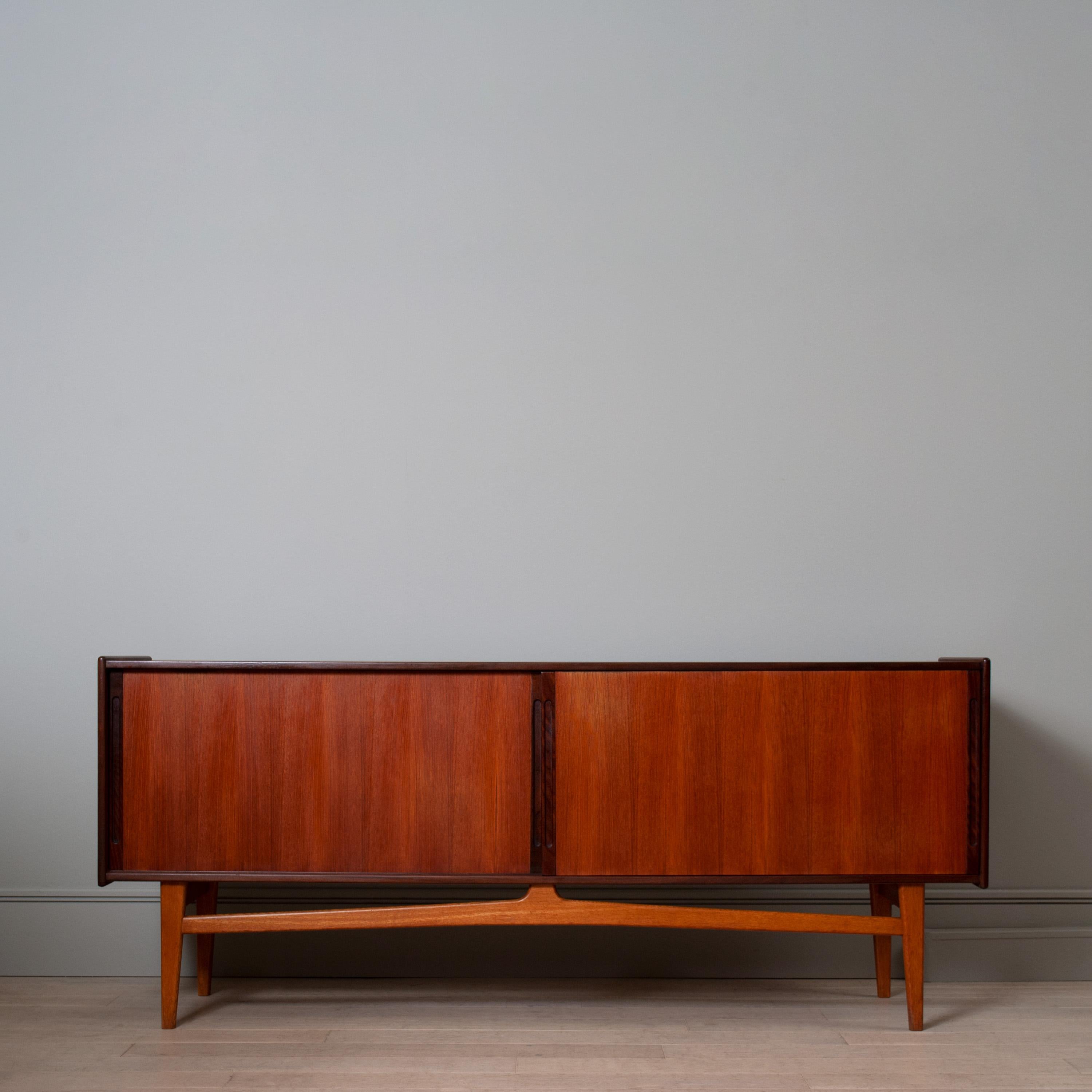 A large Scandinavian modernist sideboard - credenza made with teak and contrasting oak legs and stretcher base. The left side has an adjustable internal shelf and the right 2 drawers and a single shelf. 
Produced in Denmark circa 1960.