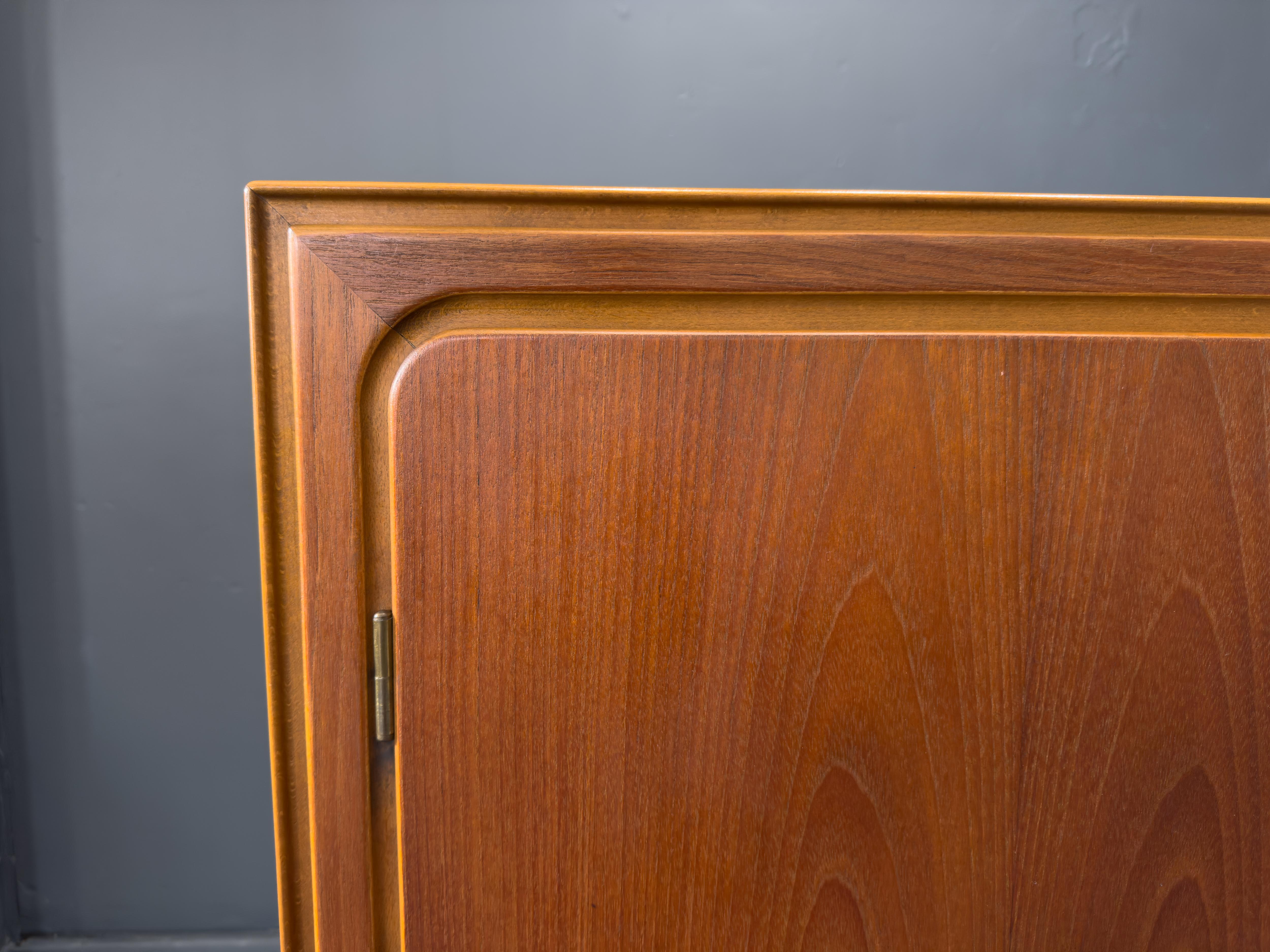 This large teak sideboard is a stunning representation of mid-century design, featuring a clean-lined silhouette, rich materials, and meticulous craftsmanship. Crafted from teak, the piece boasts a beautifully figured grain with warm, golden-brown