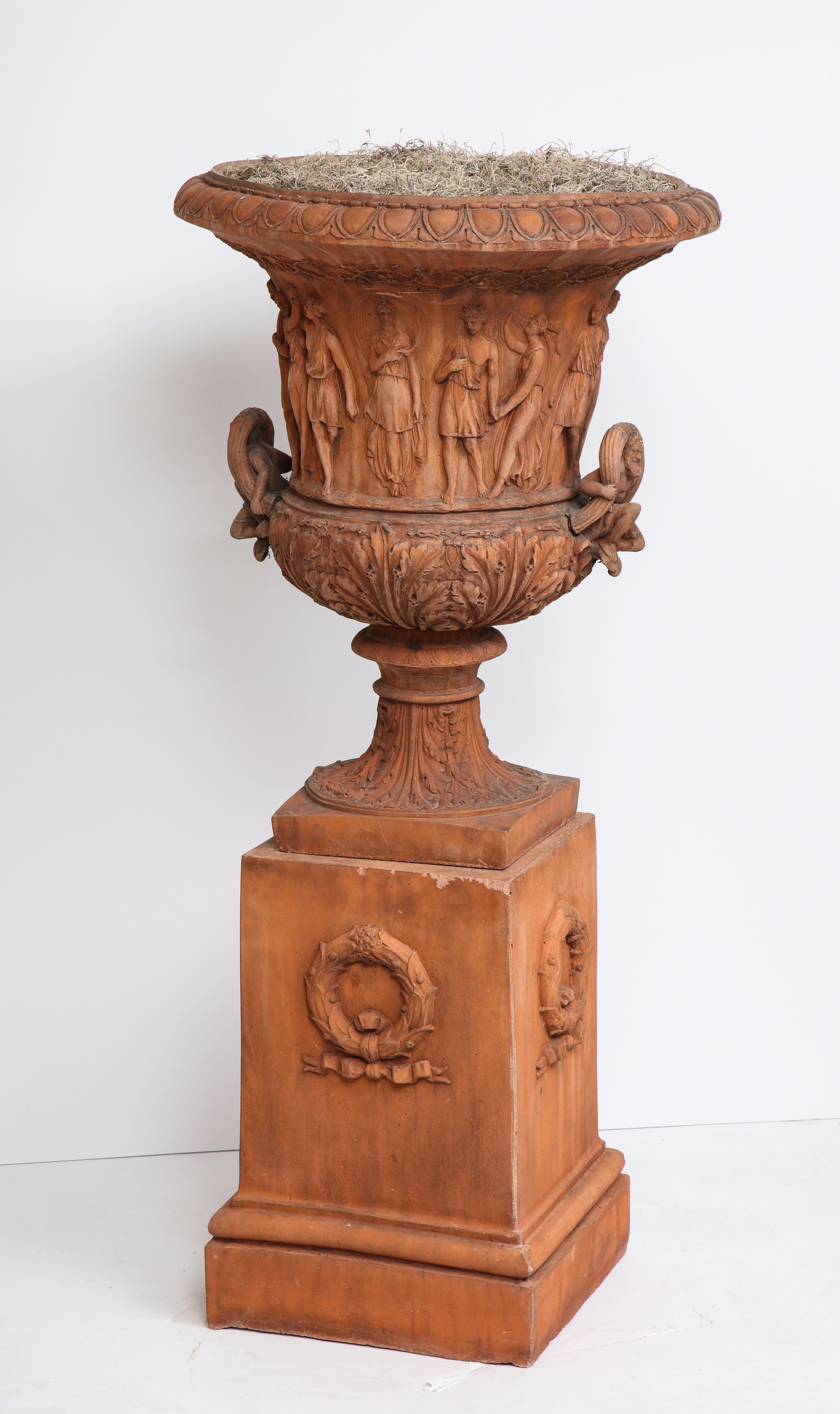 Large terra cotta urn encircled by ancient Greek figures in detailed relief on pedestal.