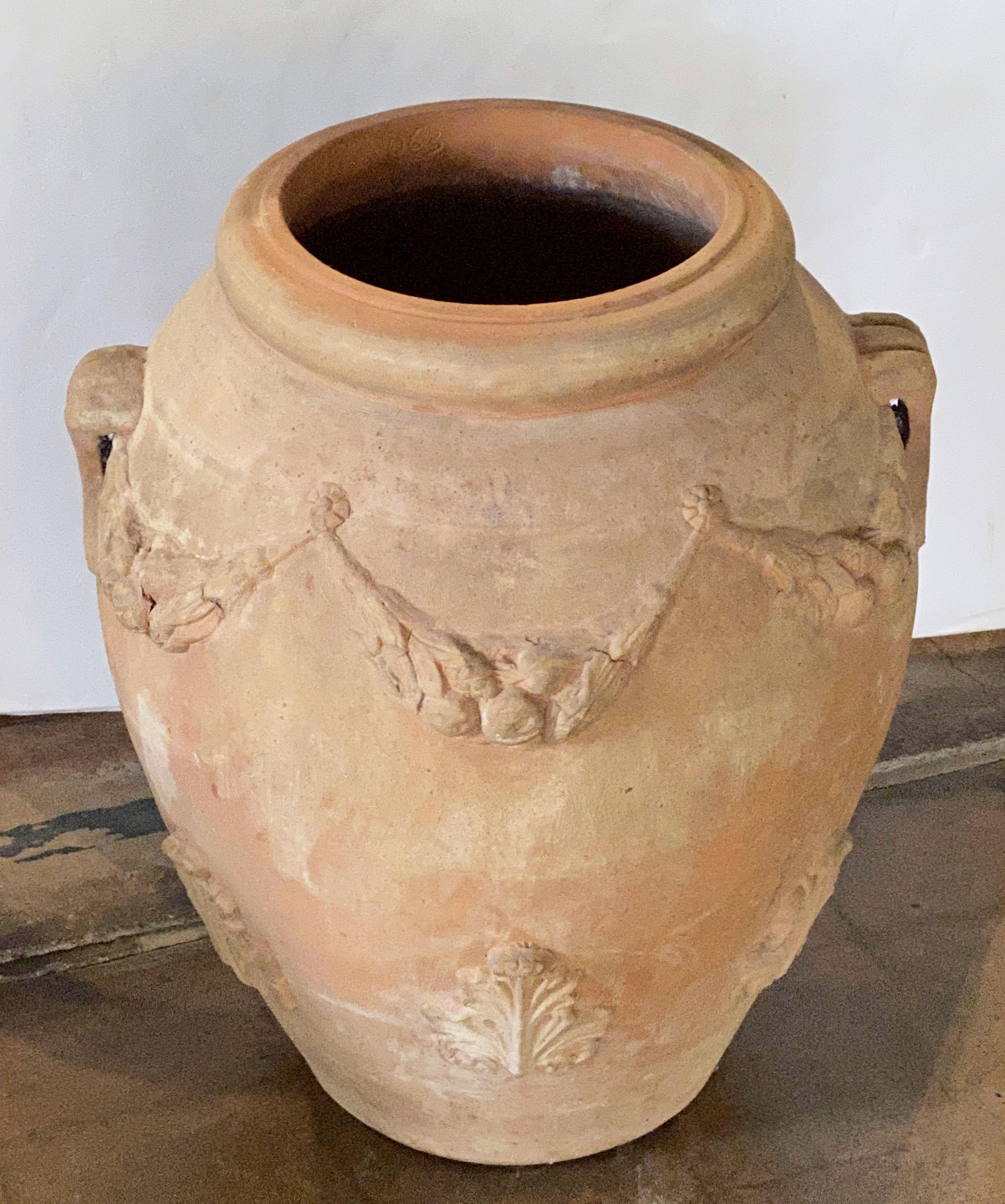 A handsome French garden pot or oil jar of terracotta earthenware pottery, featuring a rolled edge top over an ovoid body with opposing handles and decorative high-relief garlands and acanthus leaves around the circumference.

Perfect for display