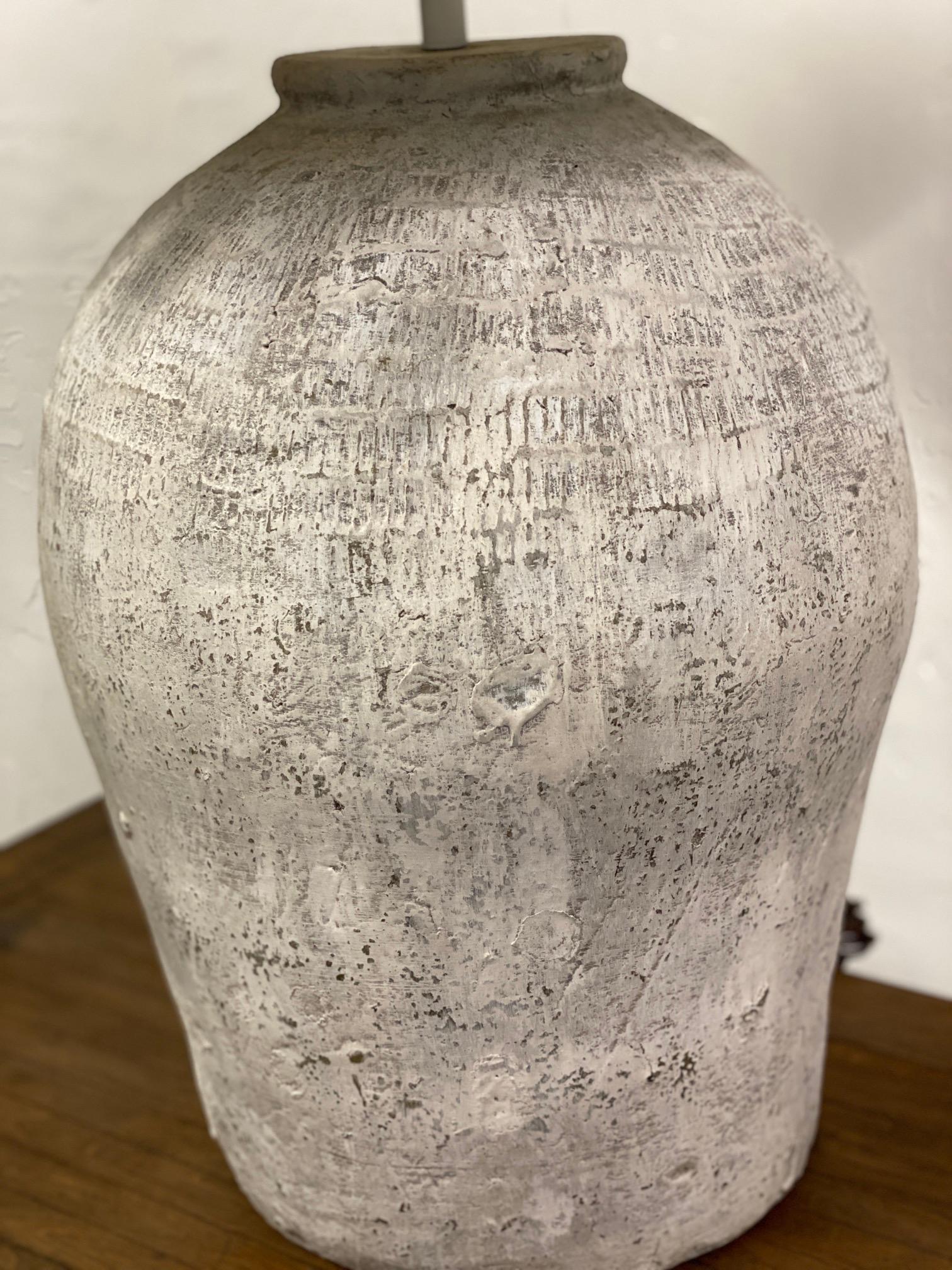 The large white painted, grey green terracotta lamp base is made from rustic vintage Chinese clay jars used for wine storage. The shape of the jar is not symmetrical since these are hand made and were used for strictly utilitarian purposes not