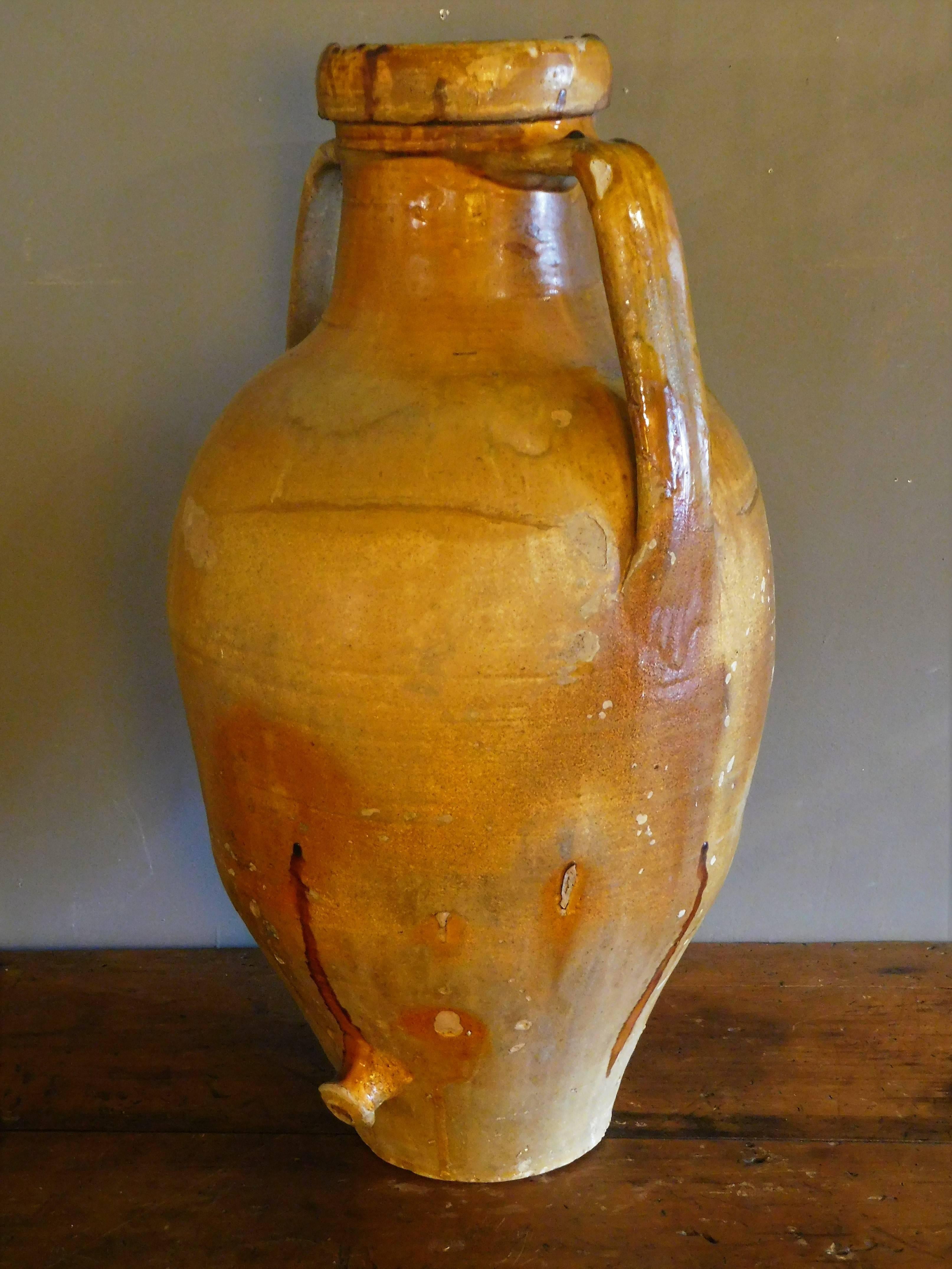 This hand-thrown rustic terracotta olive oil storage jar has large applied strap handles for convenient moving and a draining spout at the bottom for ease of use. This style of large jar is typical of southeastern Italy. Although these types of
