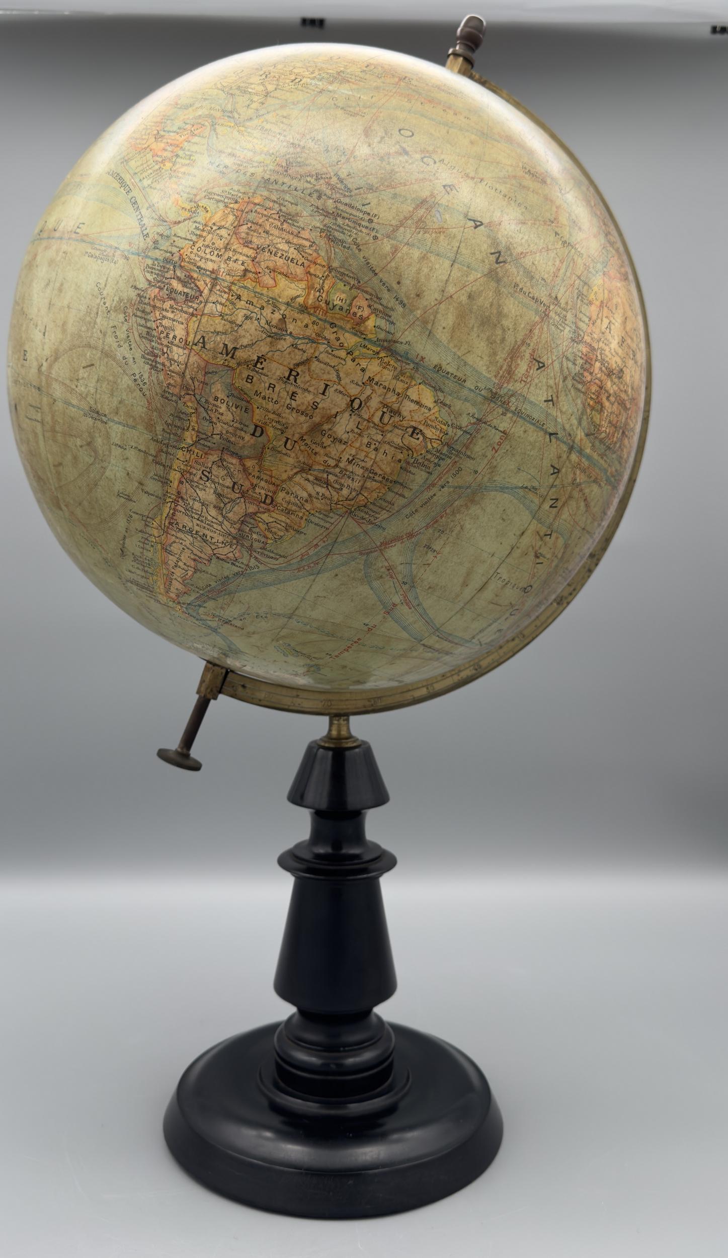 Large swiveling globe in plastered cardboard covered with printed paper.
The meridian, attached to each pole, is in engraved brass. The base is in blackened turned wood.
The colors are slightly faded, but it is in very good condition, with no