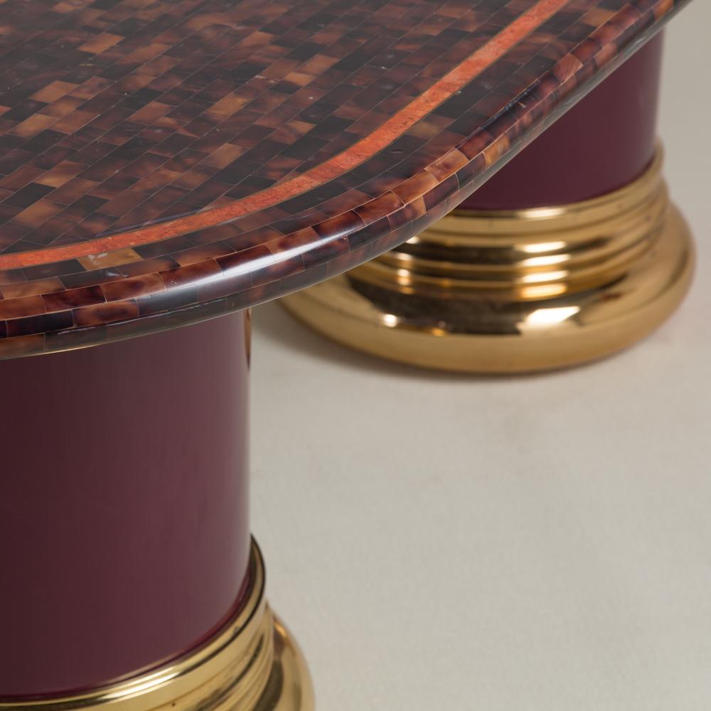 A large tessellated horn oval dining table top with a red toned and brass band edging set on a pair of brass and purple lacquered pedestal bases 1980s.