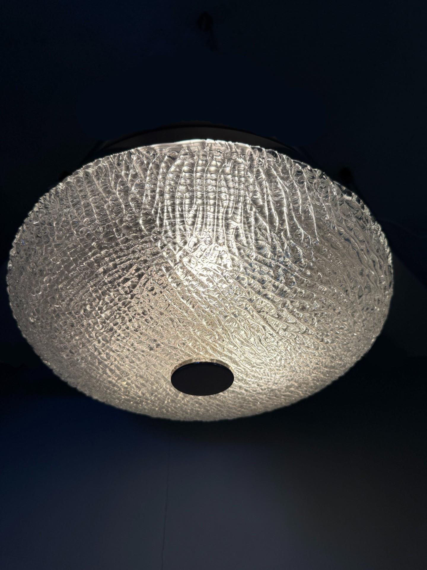 Esta impresionante lámpara de techo de cristal helado de mediados de siglo es una mezcla perfecta de elegancia y funcionalidad, que encarna el atractivo intemporal del diseño de los años sesenta y setenta. La pantalla de cristal helado texturizado