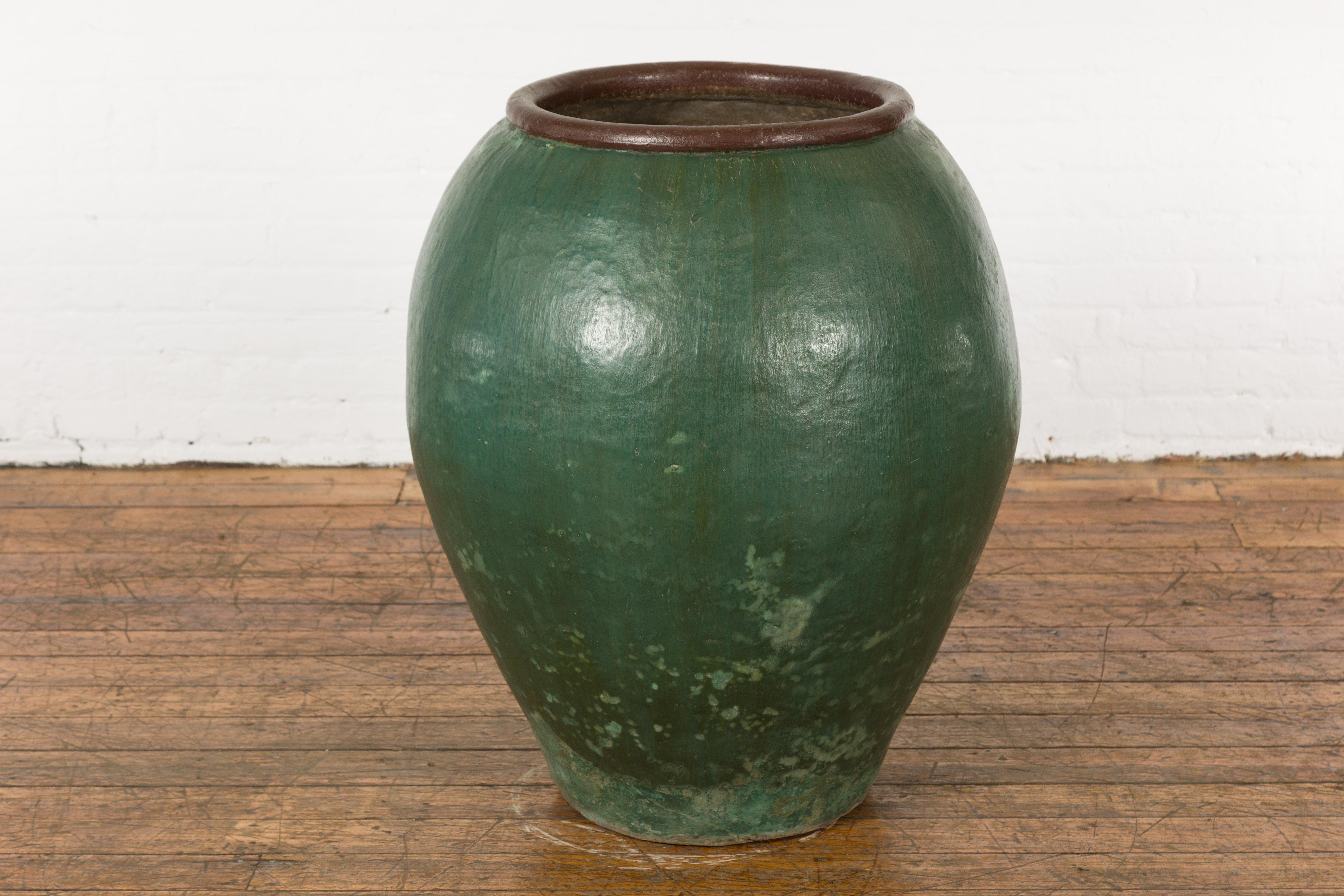 A large Thai green glazed ceramic jar from the mid 20th century with brown lip and nicely weathered appearance. Charming us with its large proportions and slightly weathered appearance revealing its age and use, this green glazed ceramic planter was
