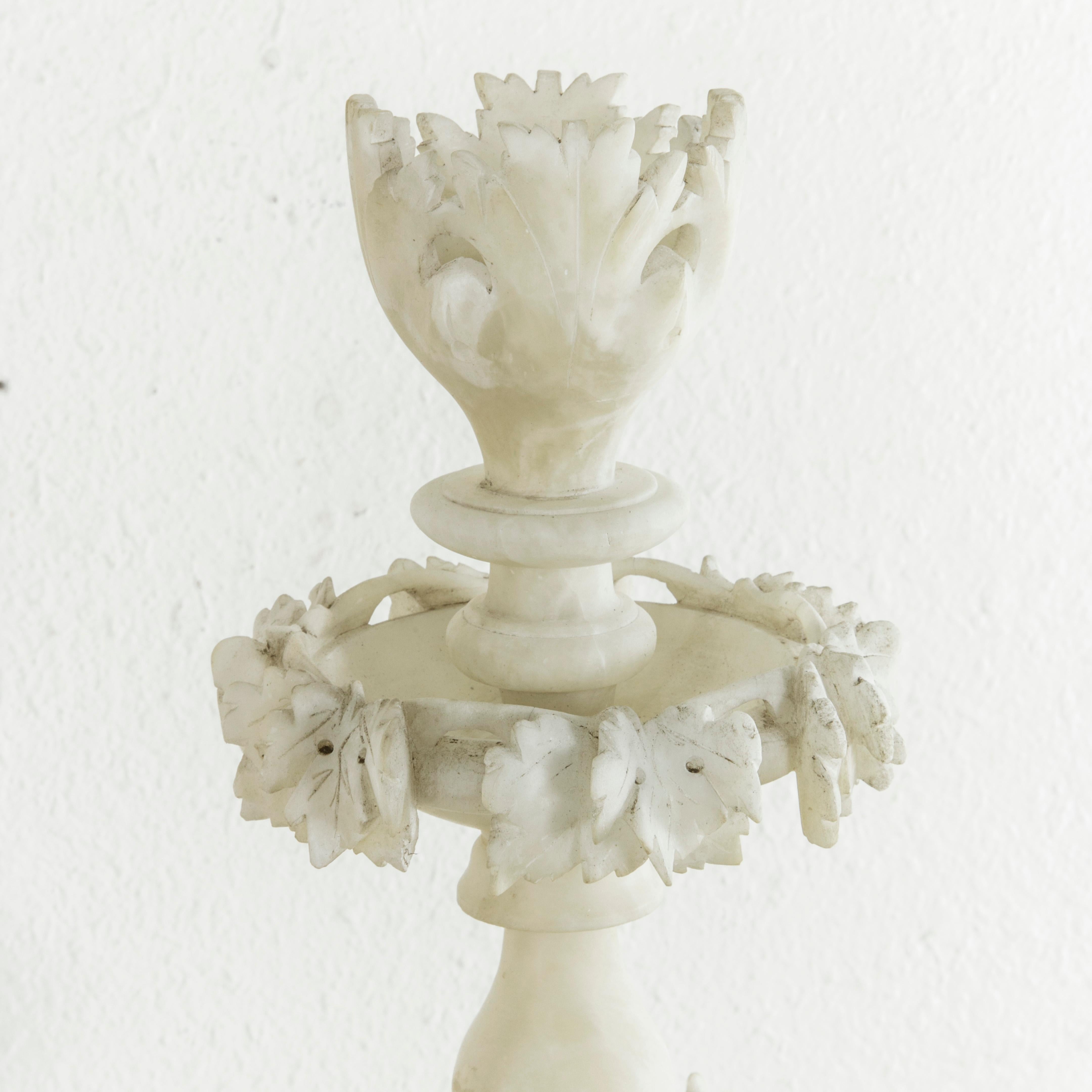 Originally used to serve candies, fruits, or nuts, this large-scale French alabaster presentation piece features three tiers, each with deep relief hand-carved detailing of grape vines and leaves around the rim. A stylized bouquet of leaves crowns