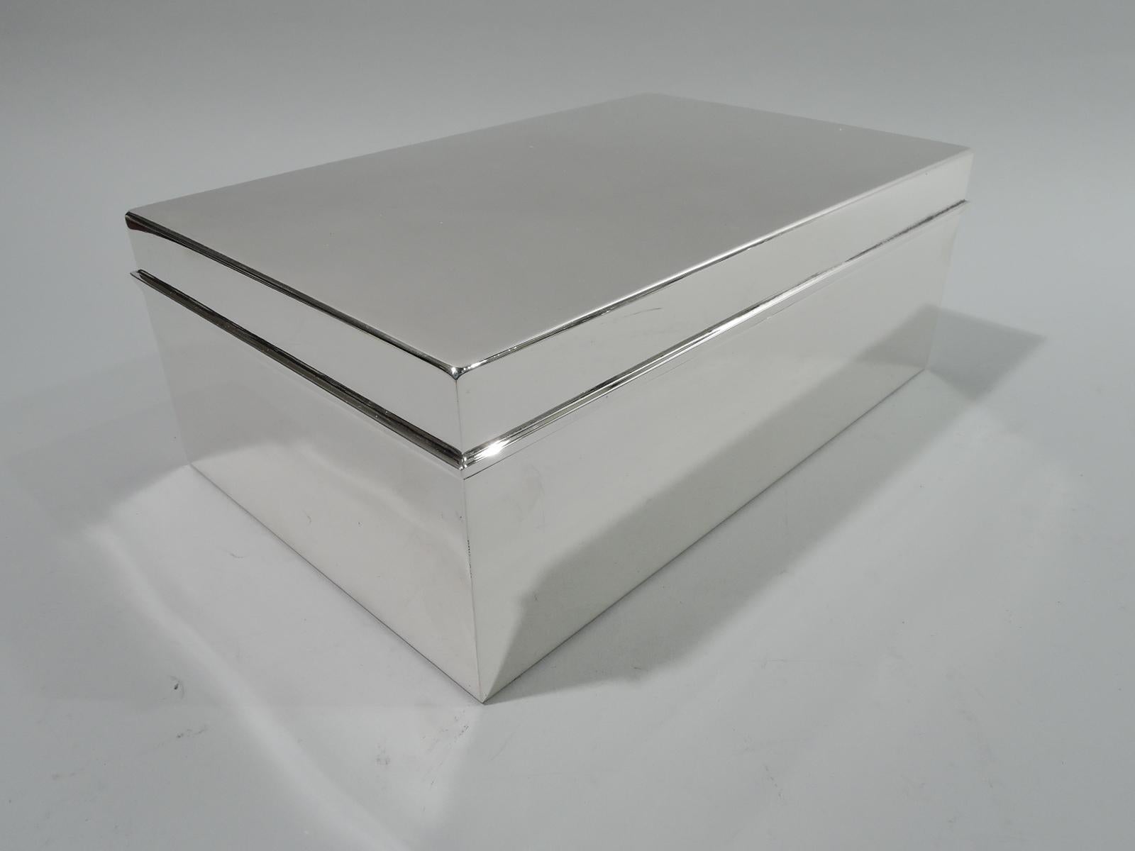 Modern sterling silver cigar box. Made by Tiffany & Co. in New York, ca 1936. Rectangular with straight sides and sharp corners. Cover flat and hinged with wraparound overhanging rim. Box interior cedar lined and partitioned. Cover interior gilt.
