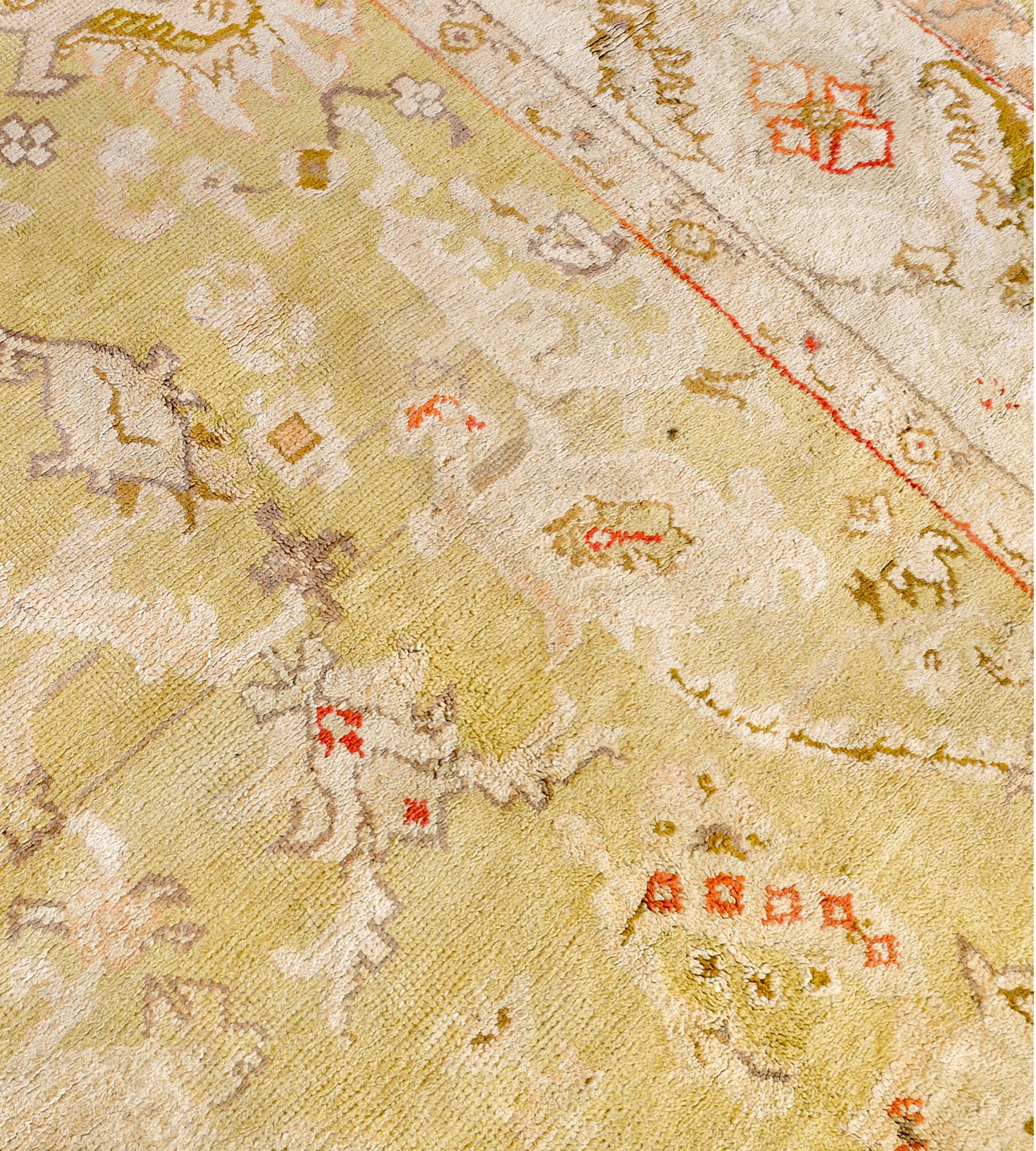 Dieser traditionelle, handgewebte türkische Oushak-Teppich hat ein chartreusefarbenes Feld mit cremefarbenen Rosetten, aus denen ein geometrisches Motiv hervorgeht, in einer kühnen elfenbeinfarbenen Bordüre aus miteinander verbundenen Rauten mit