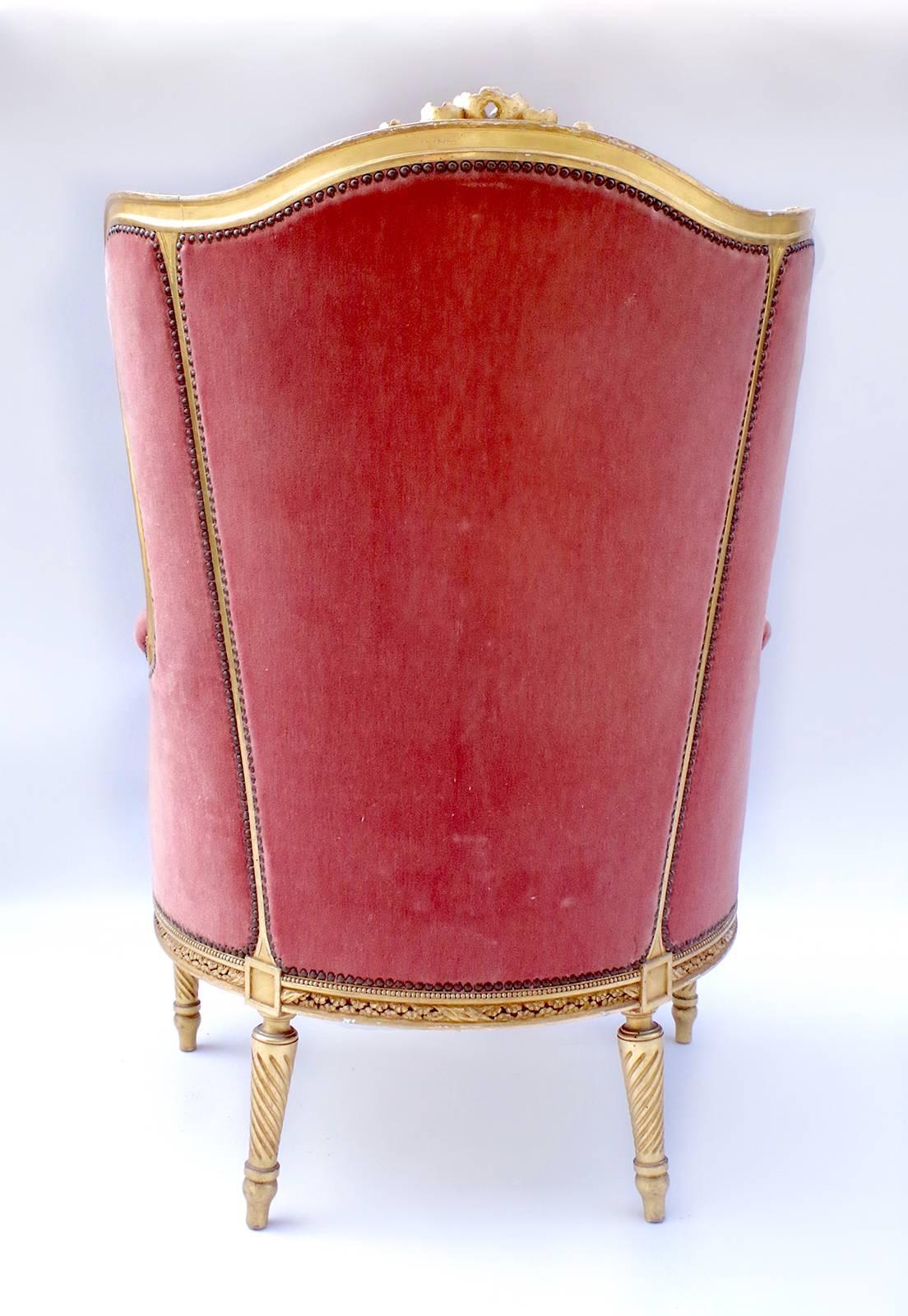 Large transition Louis XV / Louis XVI style cabriolet wing chair. Moulded, sculpted and giltwood model, standing on four tapered and fluted legs. The apron, the arm-rests, the uprights are decorated by flowers, ribbons and acanthus leaves. Red