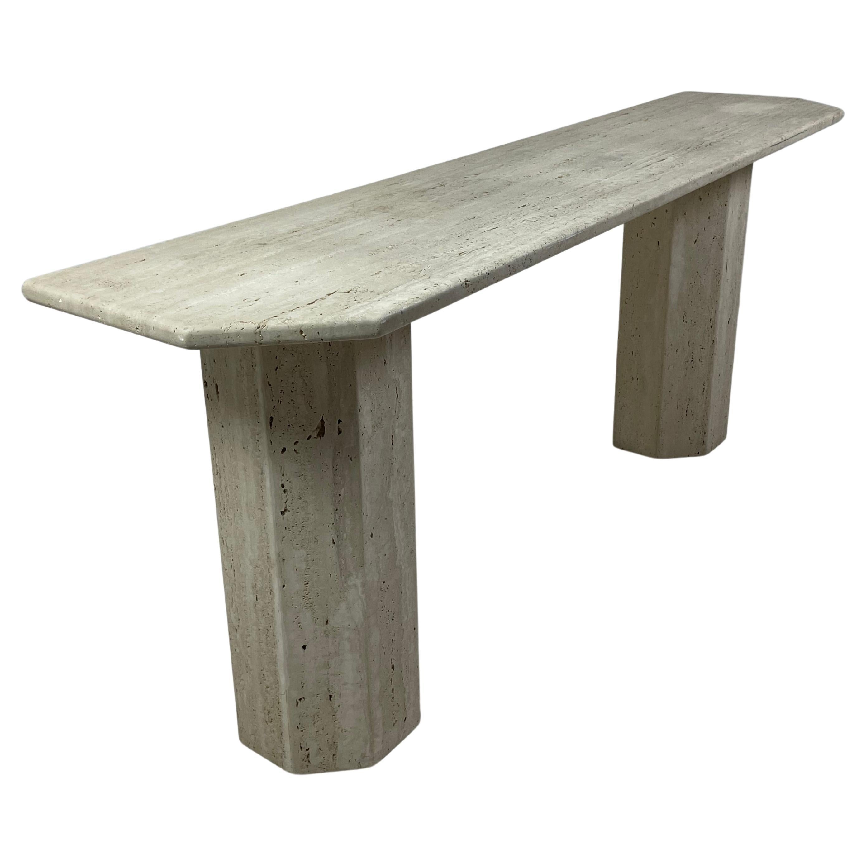 Large travertine console dating from the 1970s and from Italy. The 3cm thick and 2 meter long top rests on 2 angularly shaped bases. This natural and mineral material provides softness through its color and texture. This console can be integrated