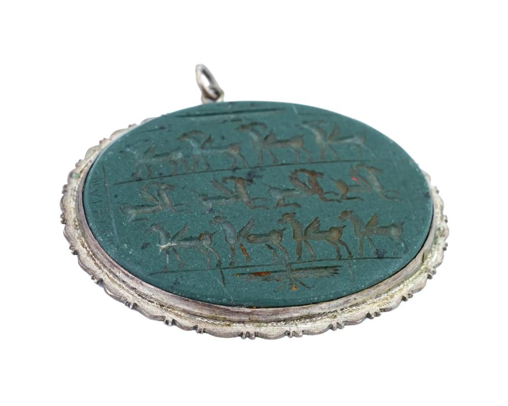 A large Turkish hand carved semi precious stone, probably Jade, intaglio pendant. The pendant is adorned with hand carved images of mythical creatures. Mounted in a Silver frame with scalloped rims. Circa: the first half of the 20th century. Total