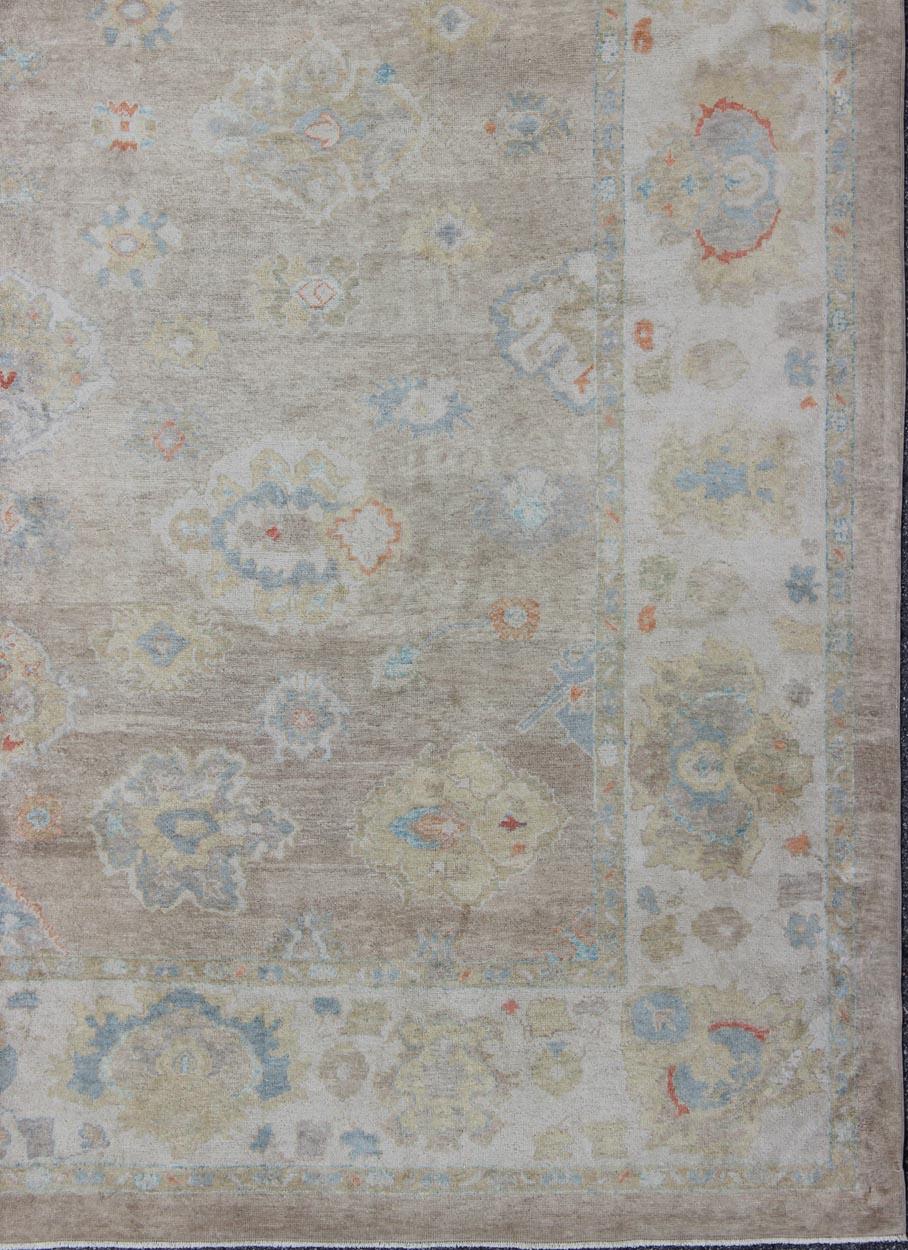 This hand Knotted, hand spun Oushak rug from Turkey features a subdued, neutral color palette and an all-over design of floral shapes, surrounded beautifully by an all-encompassing, complementary border. This piece is very versatile and will