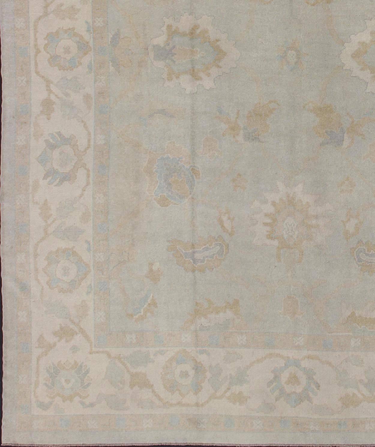 This vintage Turkish Oushak rug is remarkably elegant in both color and design. The central field of light gray plays host to a variety of large-scale blossoms in an all-over pattern with intermixed floral and palmette motifs. Complementary