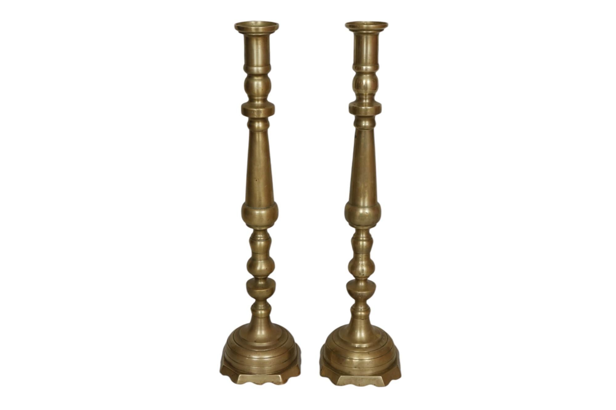 Un par de grandes portavelas de latón. Forma tradicional con columnas torneadas con balaustres cónicos y nudillos. Las bases octogonales en forma de campana están decoradas con líneas biseladas y acabadas con un borde serpenteante. Dimensiones por