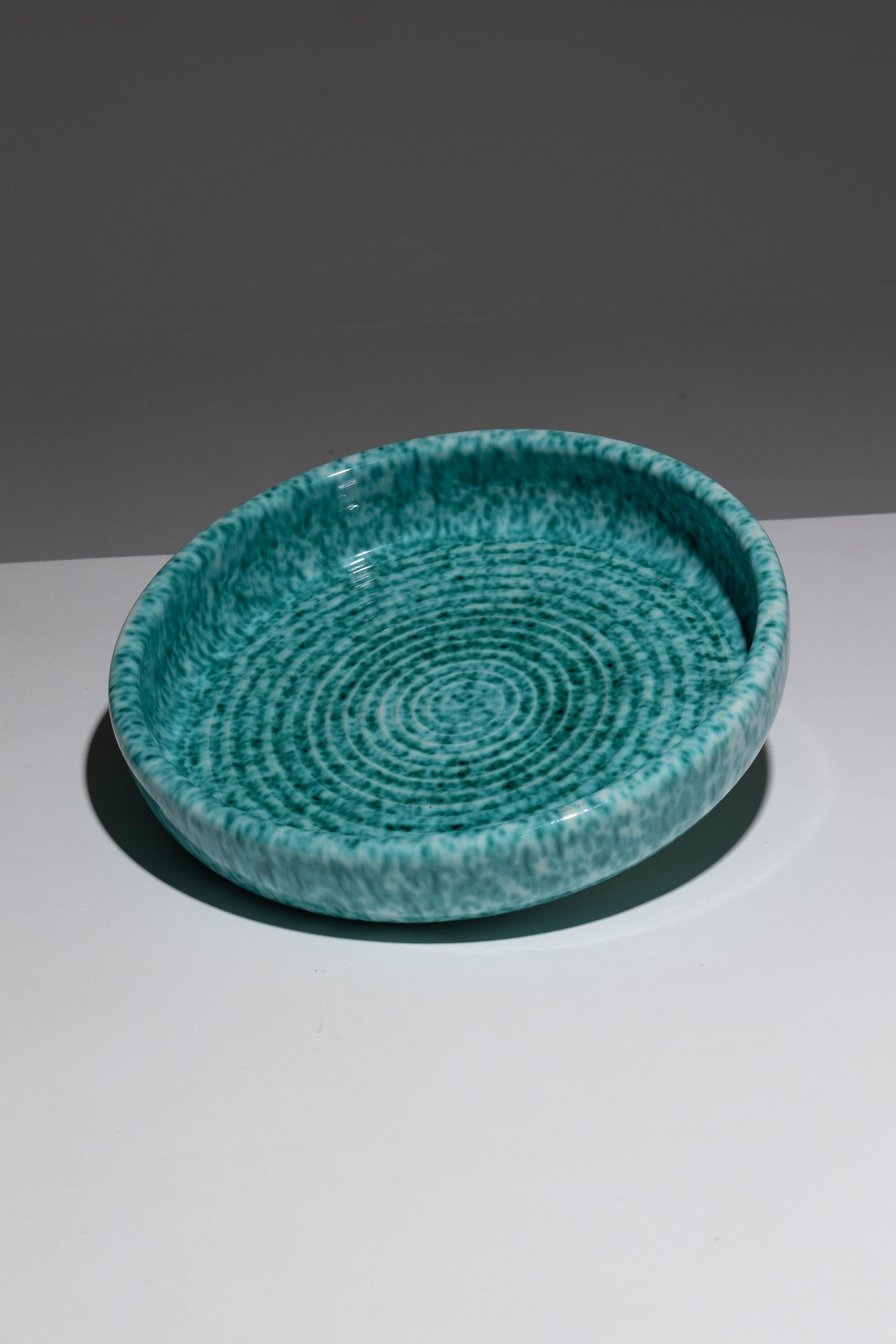 Gran frutero o plato de loza turquesa de Fernand Elchinger, años 50. Bajo el vidriado verde cobrizo, moteado de blanco, quedan marcas decorativas de torneado. Marca impresa: 'Céramique d'Art / Elchinger Fils / Soufflenheim / Francia'. Muy buen