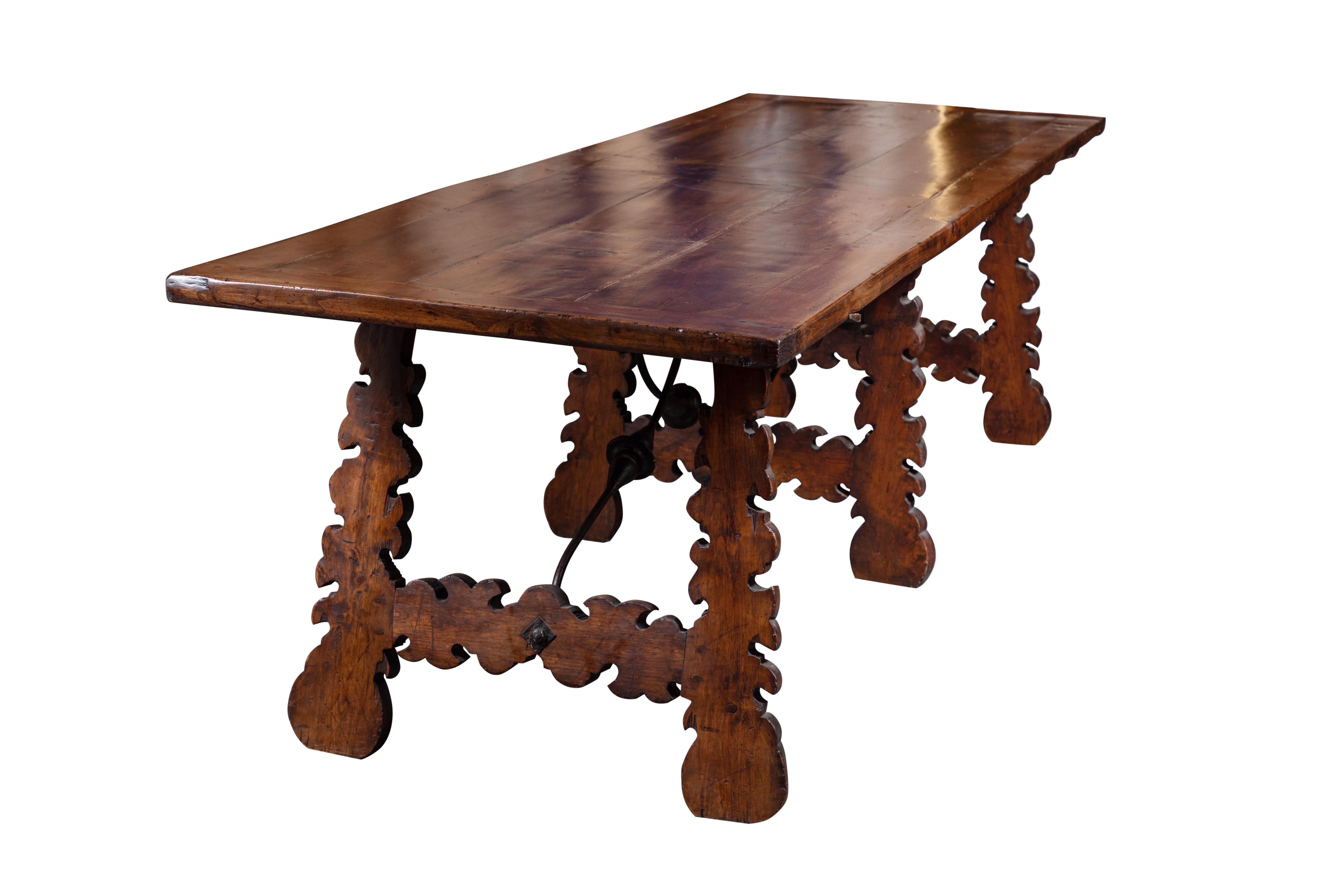 Carved walnut dining table featuring a hand forged, wrought iron stretcher and three sets of undulating trestles.