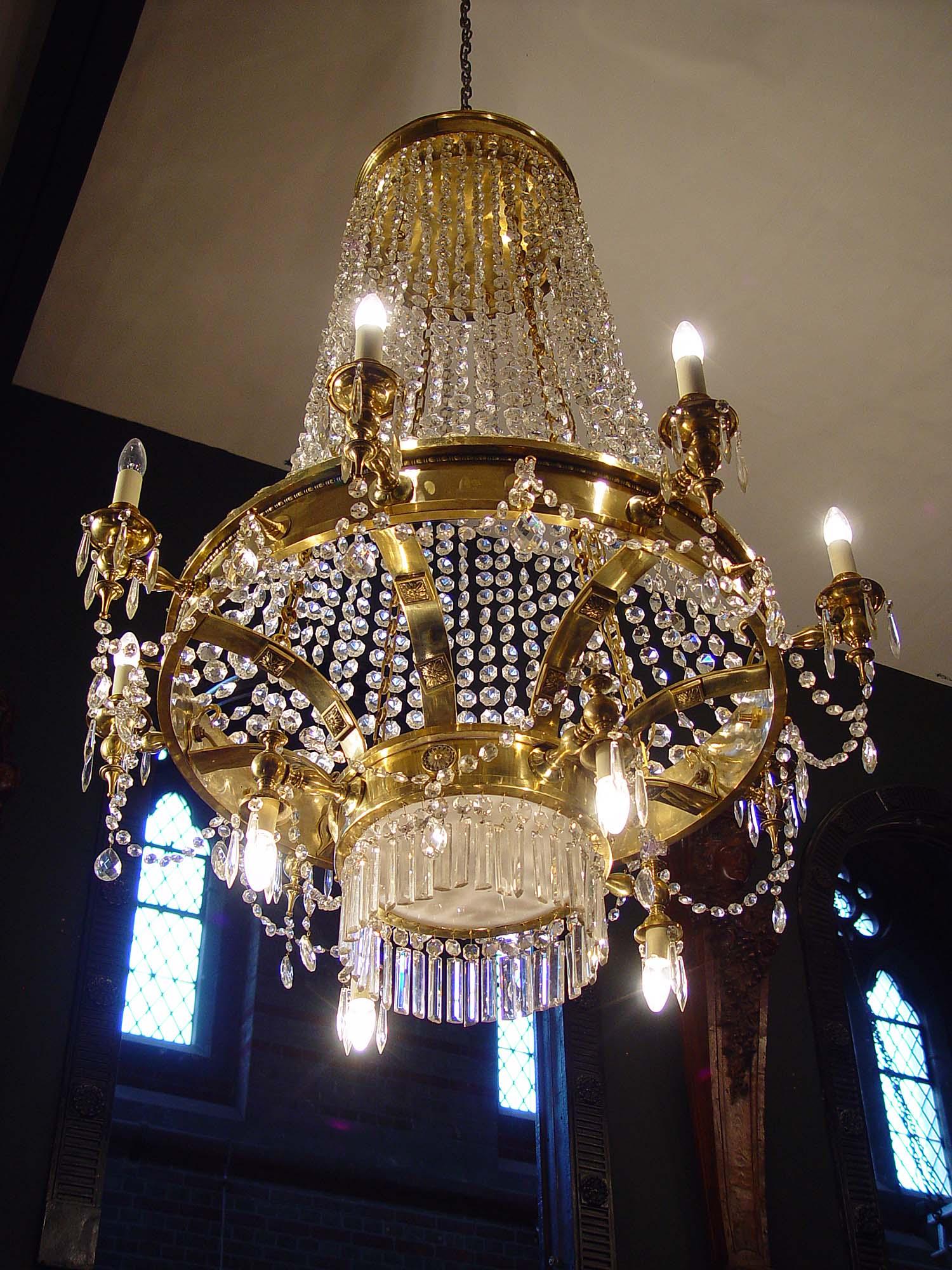 A large twelve-light 20th century gilt brass and crystal chandelier in the English Regency manner. The main rim with smaller lower rim applied with candle branches and strung with glass beads and pendants. The brass structure decorated with rosette