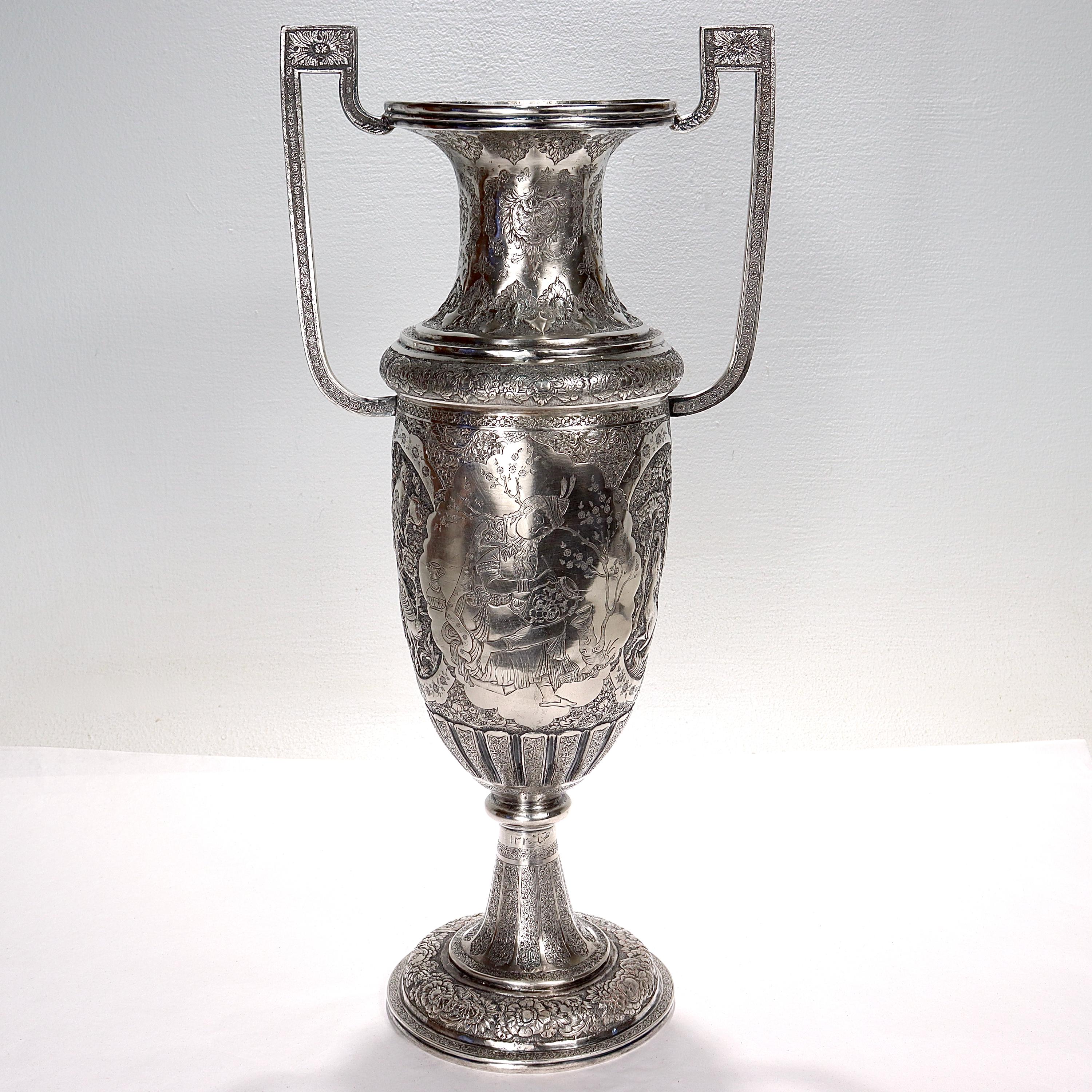 A fine large old or antique Islamic silver vase.

With twin handles and supported on a pedestal foot. 

The vase has figural incised decorations to cartouches on both the front and verso. The front cartouche depicts an artist decorating a vase (or