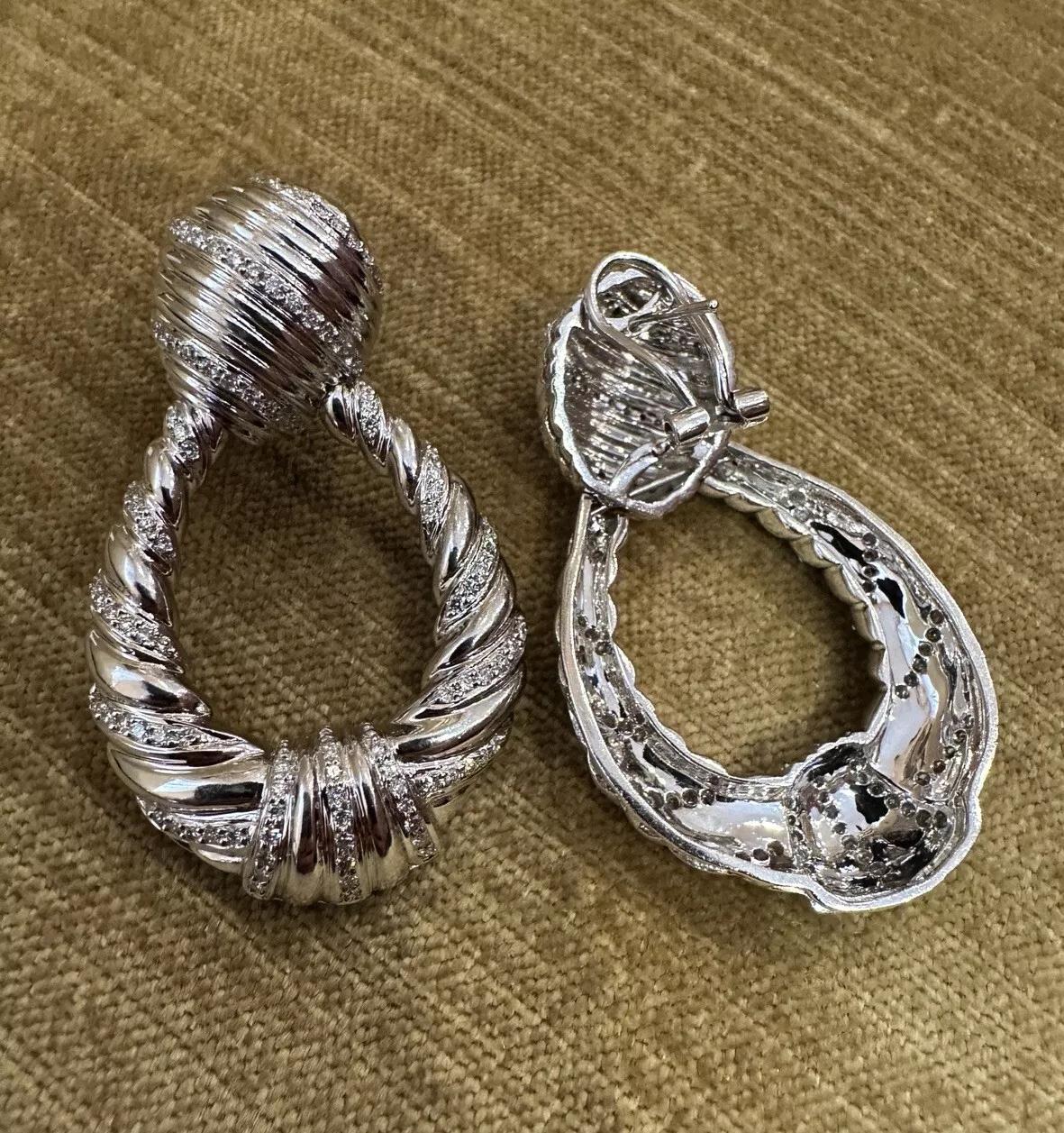 Large Twist Diamond Door-knocker Drop Earrings in 18k White Gold 

Large Twist Diamond Door-knocker Drop Earrings feature Natural Round Diamonds set in 18k White Gold with a twisted door-knocker design. The earrings are secured by an Omega back