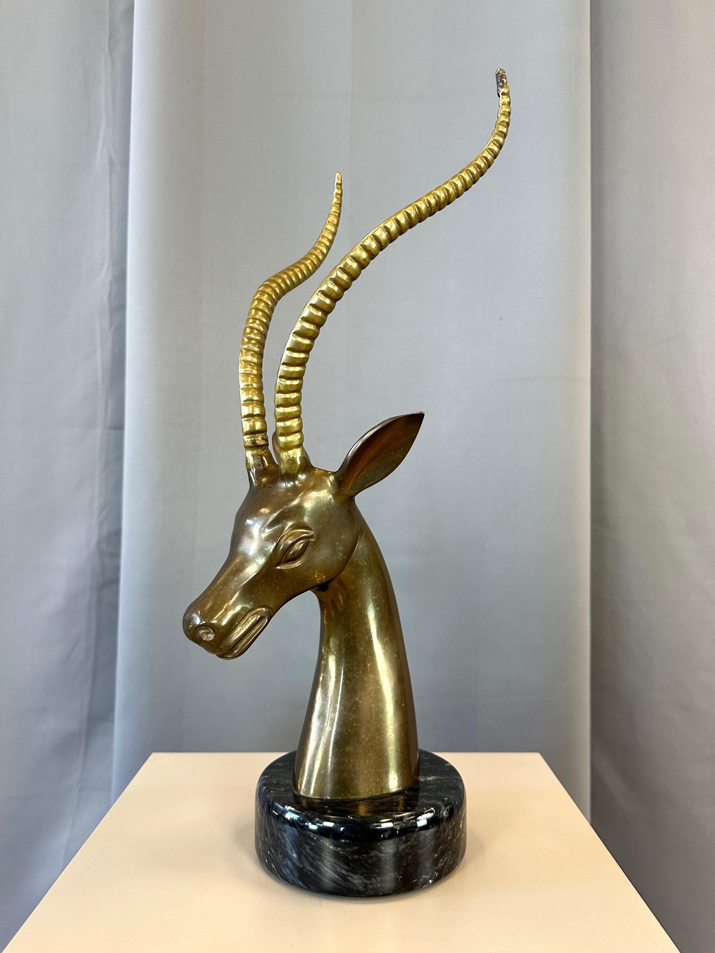 A large and striking 1970s Hollywood Regency-style brass impala bust sculpture on black marble base.

Elegant depiction of the iconic African antelope species features slender lyre-shaped ridged horns of polished brass atop a head and long, graceful