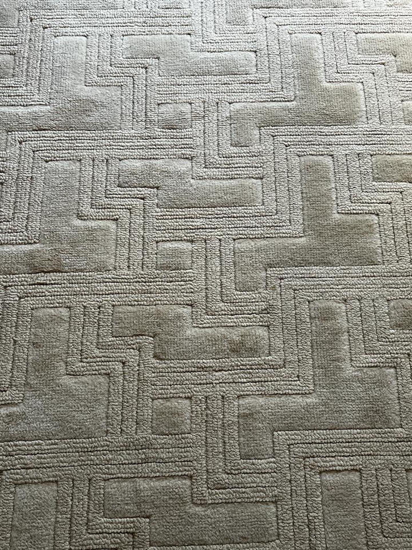 Large knotted and tufted unbleached wool rug with geometric designs of mazes. Label on the back 