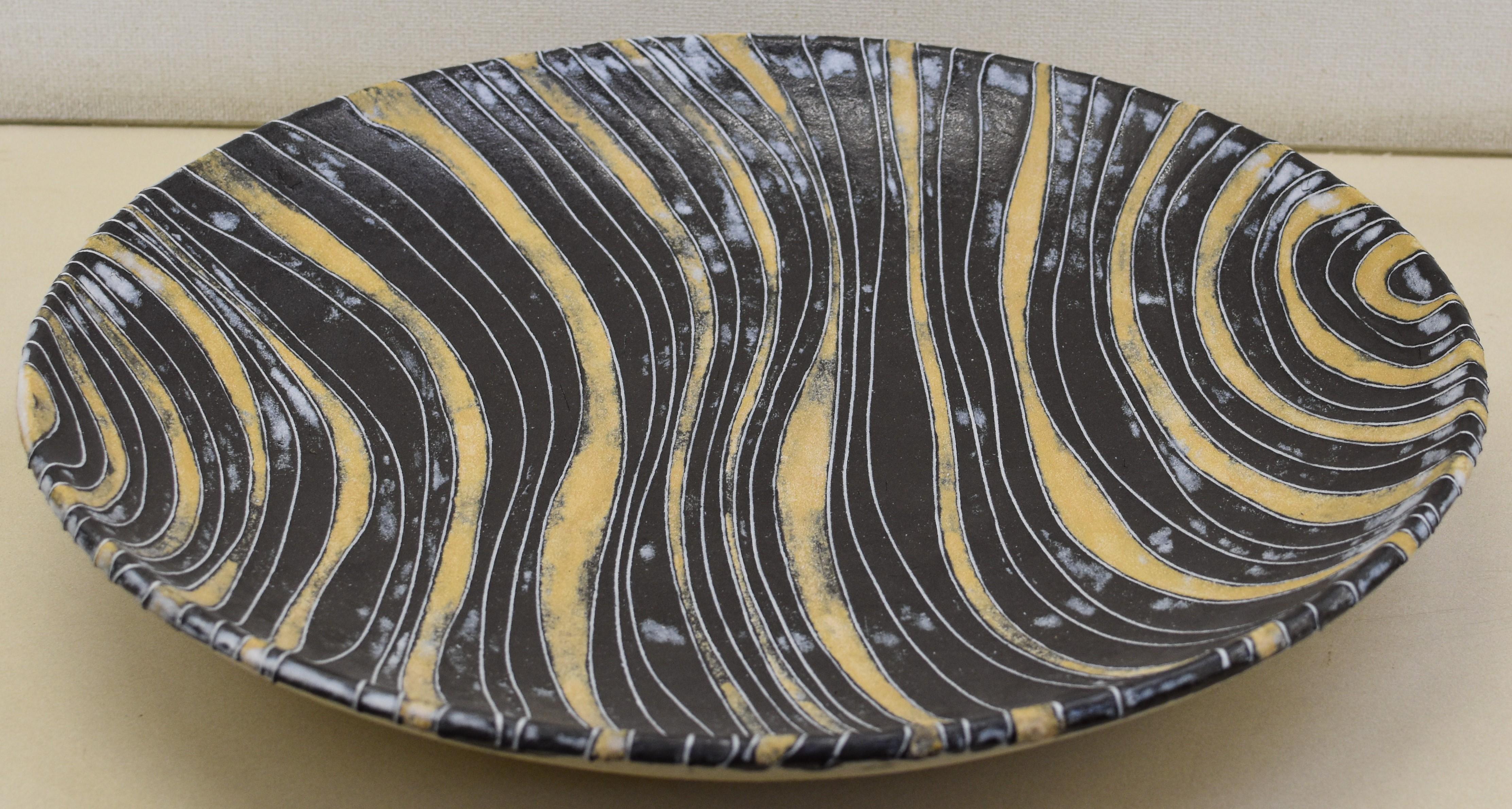 This large unglazed contemporary earthenware deep charger in black and yellow, by a master Japanese ceramic artist employs slip inlay techniques (known as zogan) to create a dynamic canvas of flowing color and movement. Located on the foothills of
