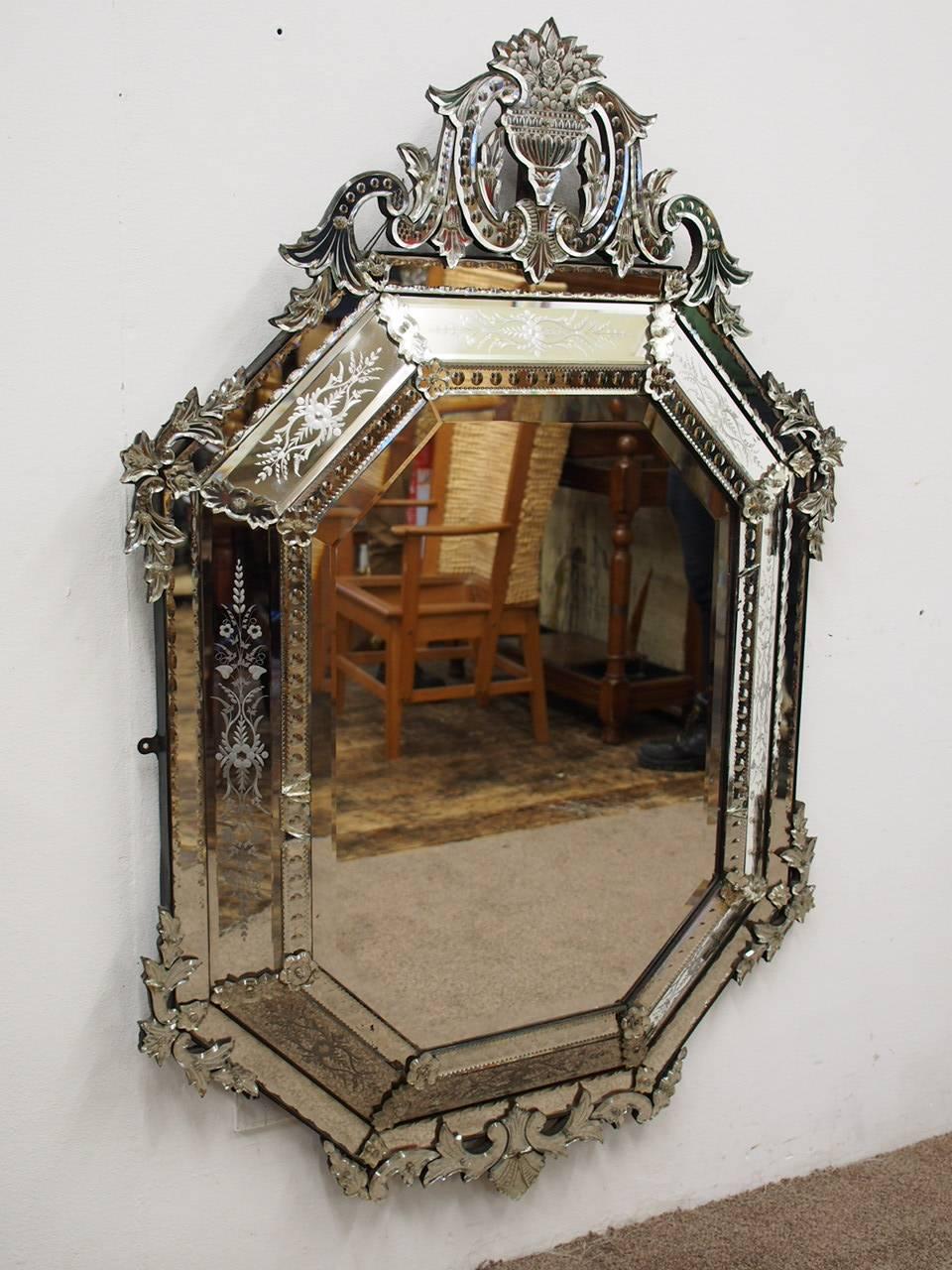 Large Venetian etched glass wall mirror, circa 1920. The bevelled octagonal mirror plate lies within eight foliate etched margin plates and is surmounted by an urn and foliate scroll cresting. It has further foliate scrolls down the sides and has an
