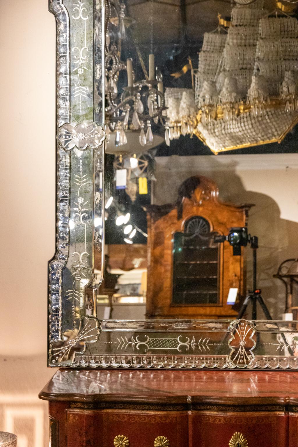 Circa 1920s Venetian mirror of large proportion in excellent state of preservation. The mirror is constructed with etched glass accented with c-scrolls and scalloped trim throughout the perimeter of the frame. Made in either France or Italy. Please