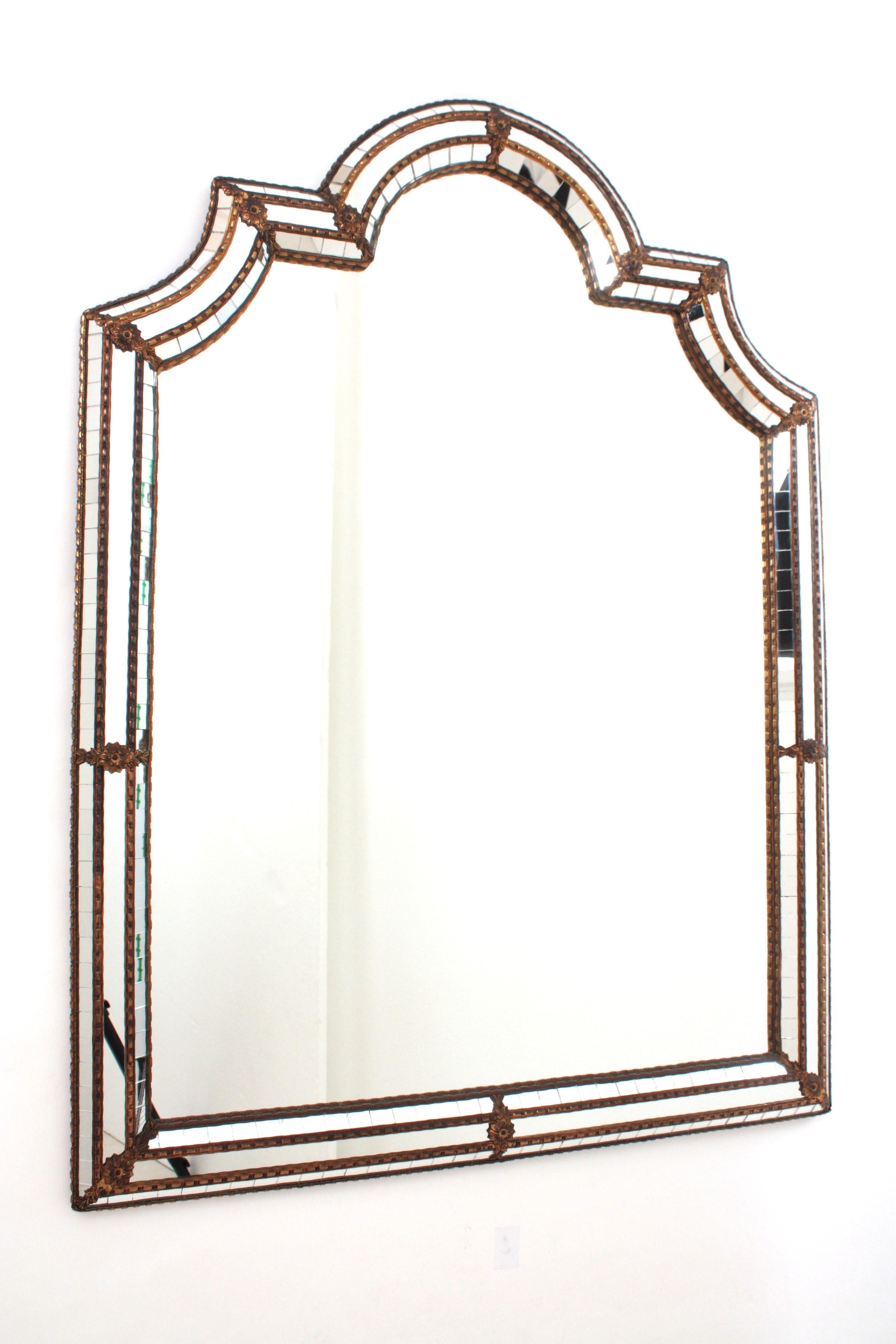 Venetian style arch top mirror with gilt metal accents, Spain, 1960s
This glamorous mirror features a triple layered mirror frame made of brass. The frame has three layers of decorative paneled mirrors. The central layer has mirror glass panels and