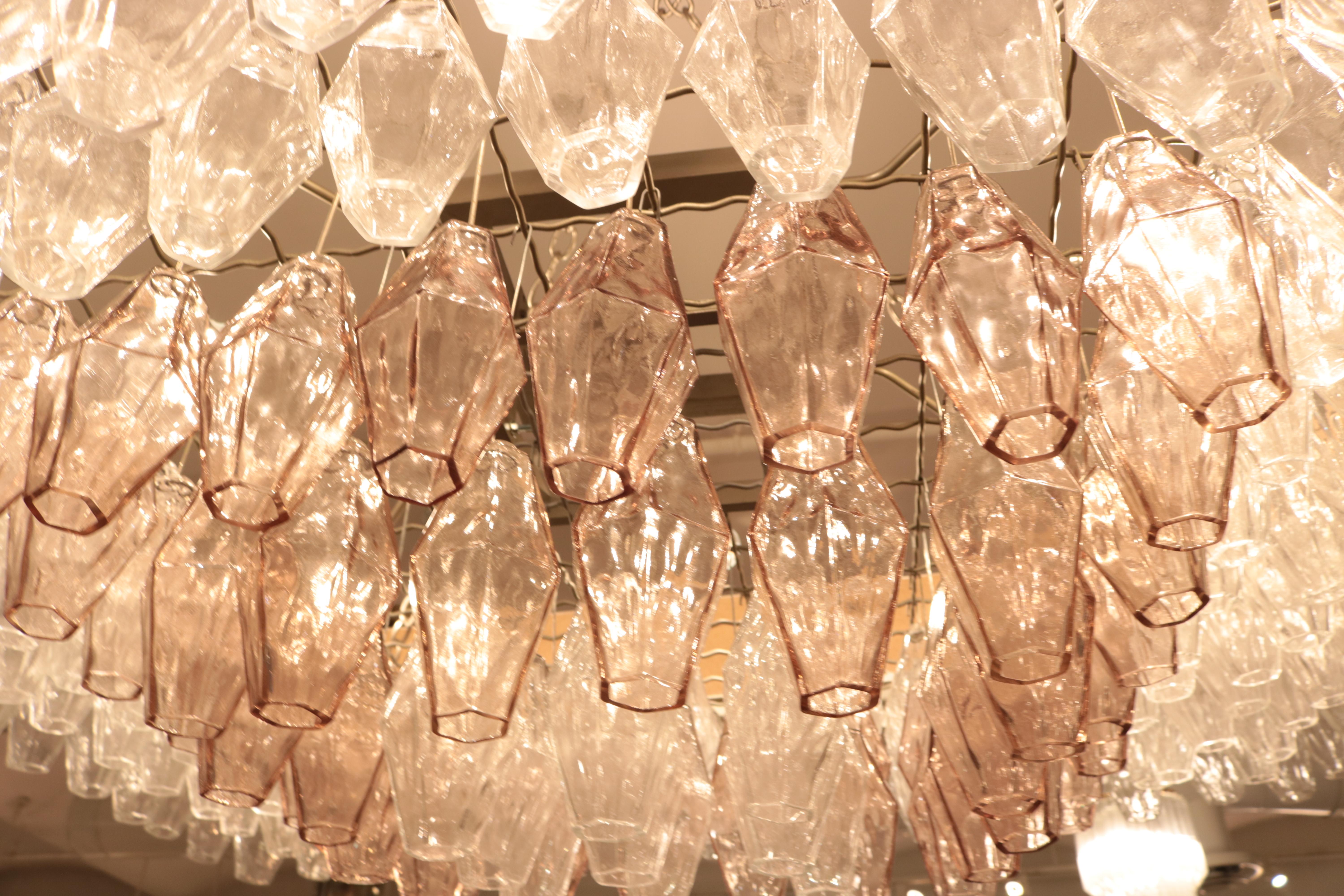 A large Venini glass light installation. Numerous clear and rose colored glass cylinders hang from a metal wire frame lit with eight lights from above. Enclosed in a modern wooden enclosure.