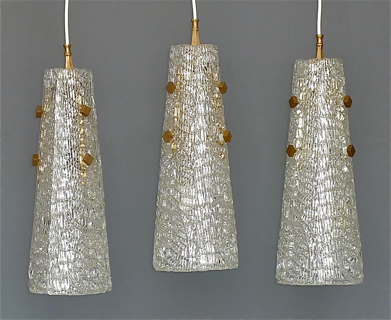 Rare and early set of three Paolo Venini midcentury pendant lamps of slightly iridescent and textured Murano ice glass, Italy circa 1950s. The large lights are made of three glass petals forming a cone shade and beautiful patinated brass details.