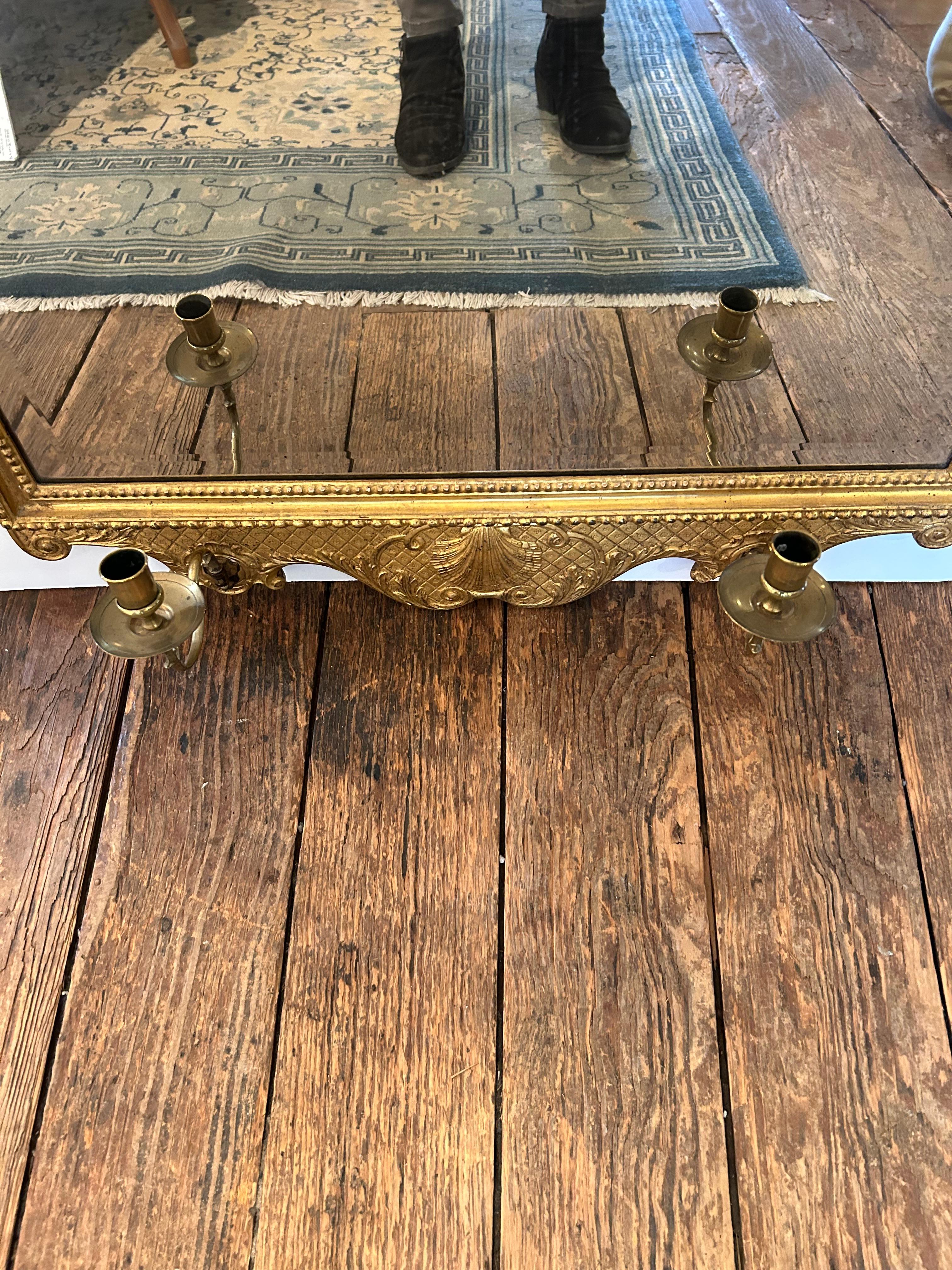 Unusual and lovely large vertical vintage mirror having giltwood frame with two candle sconces.  The sconces swing left and right and protrude 5”.  Mirror is aged and bevelled.
