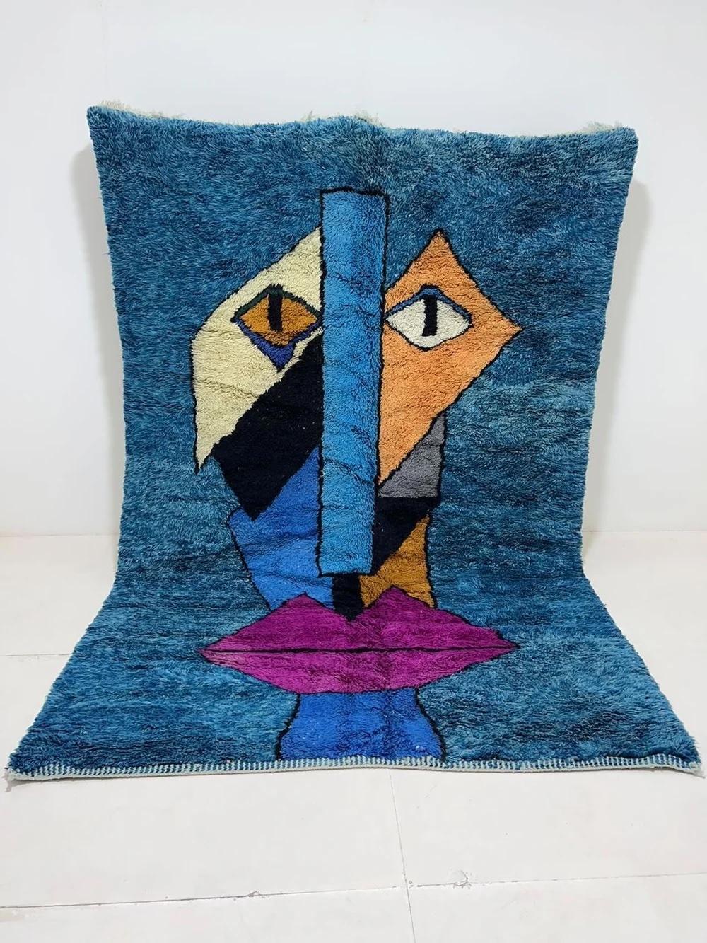 This vibrant, funky handwoven Moroccan rug was made by hand by skilled artisans in the Atlas Mountains using the highest quality M'Rirt wool. It features an abstract, colorful postmodern face design in a unique color palette atop a bold blue wool